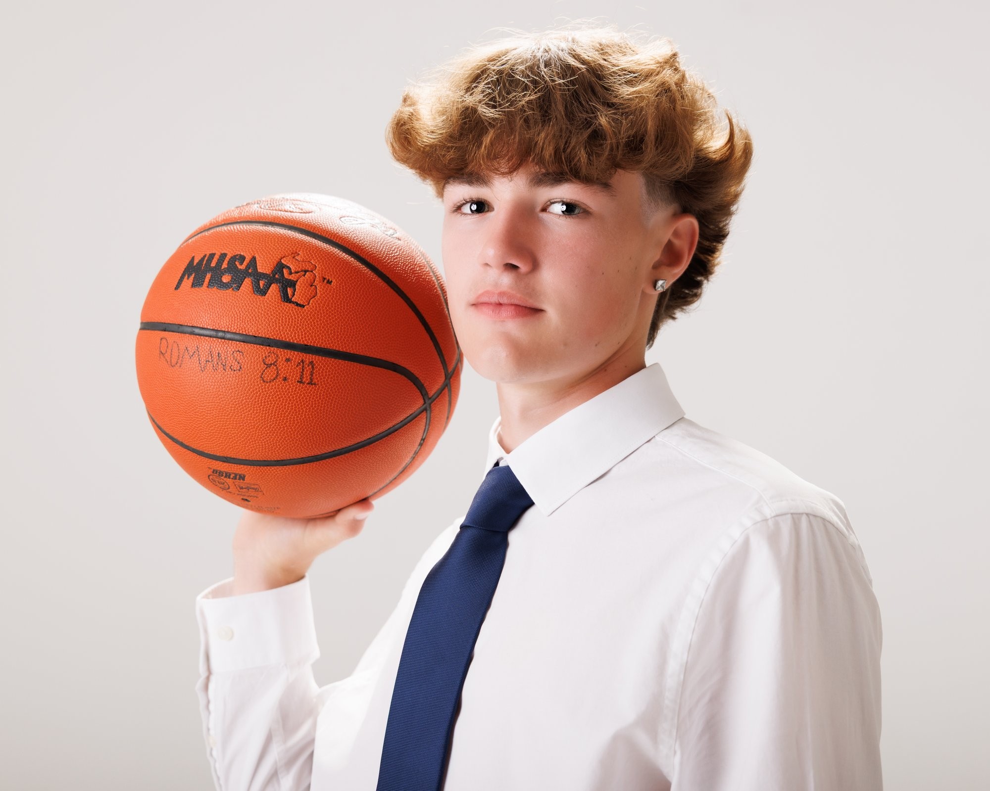 Evan in a navy suit and tie, smiling confidently against a dark studio backdrop for senior photos