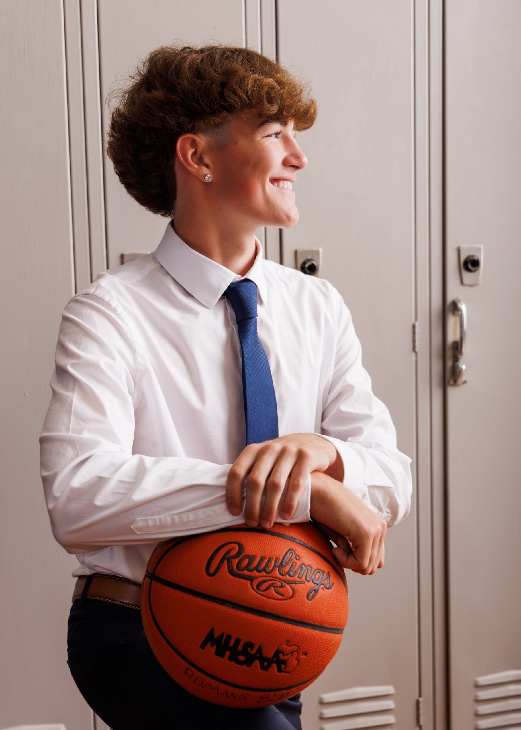 Evan in a navy suit and tie, smiling confidently against a dark studio backdrop for senior photos