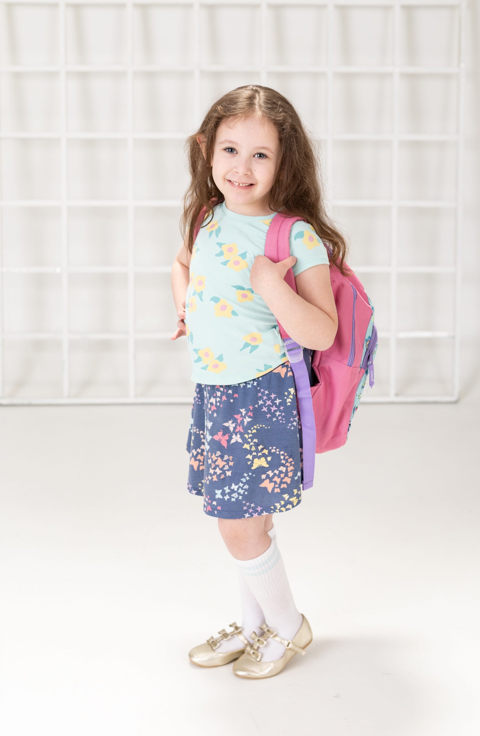 Bonnie posing by blue school lockers with pink backpack, smiling for the camera