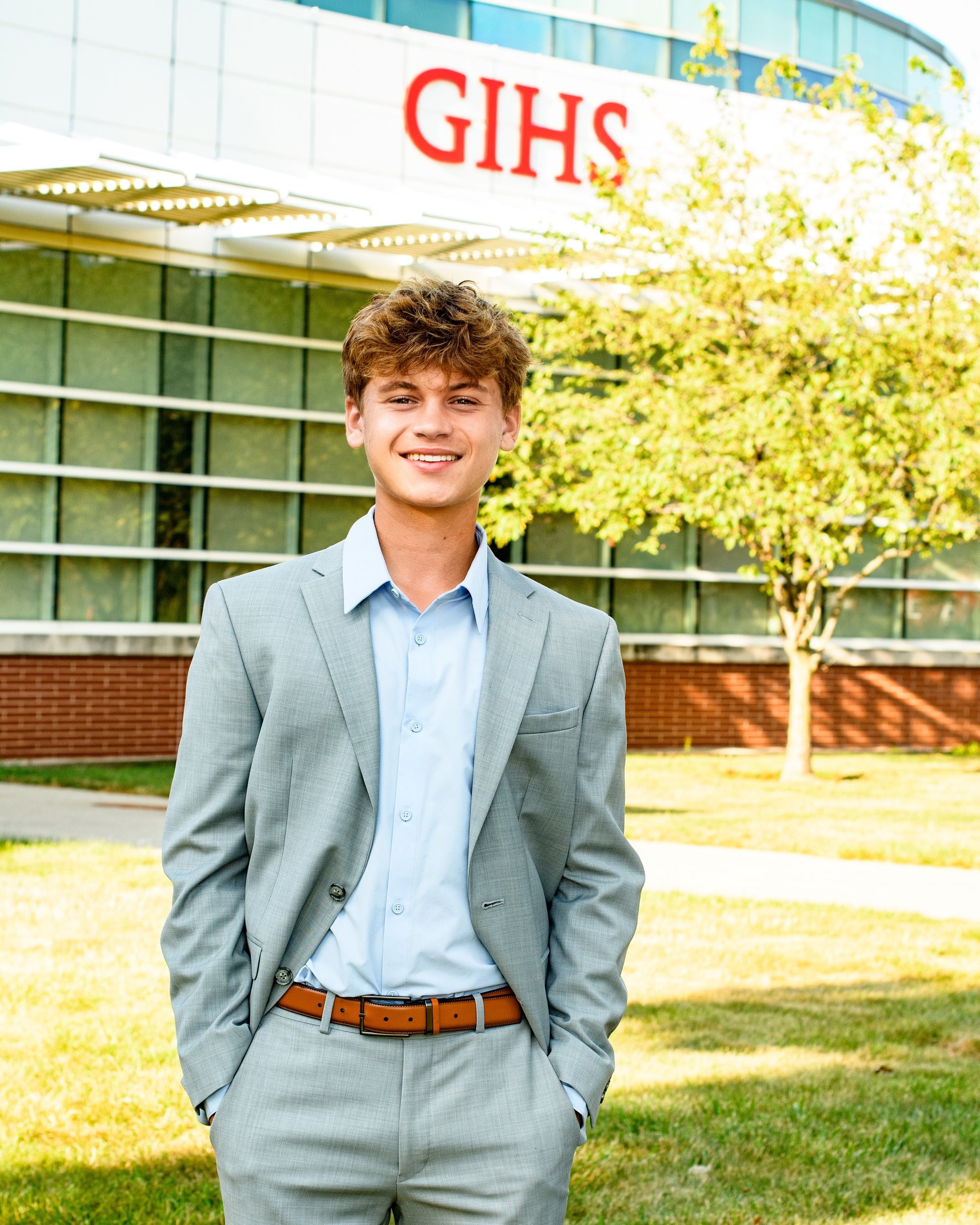 Student portrait during Grosse Isle High School senior photo location session, wearing striped shirt and gray pants on grass