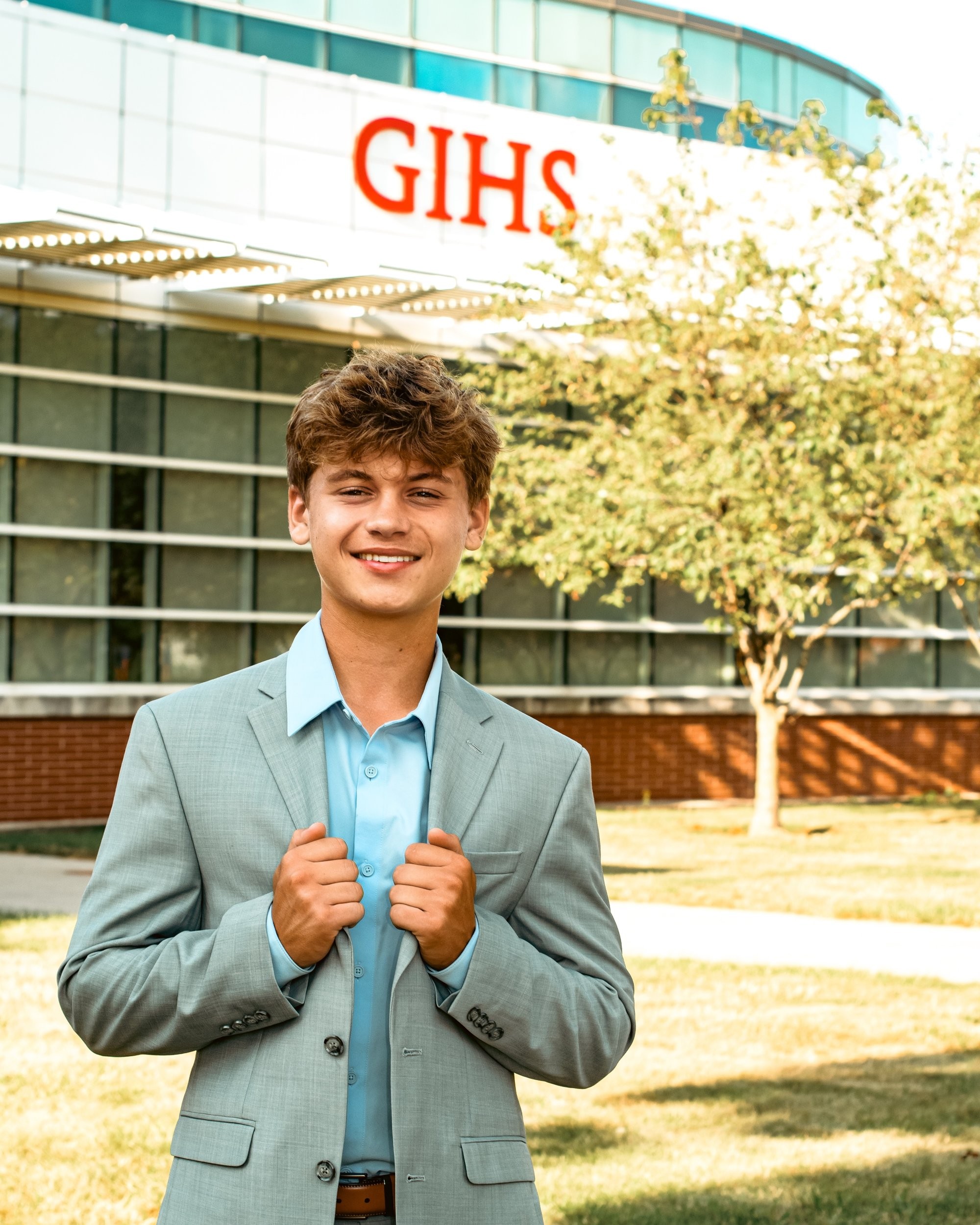 Student portrait during Grosse Isle High School senior photo location session, wearing striped shirt and gray pants on grass