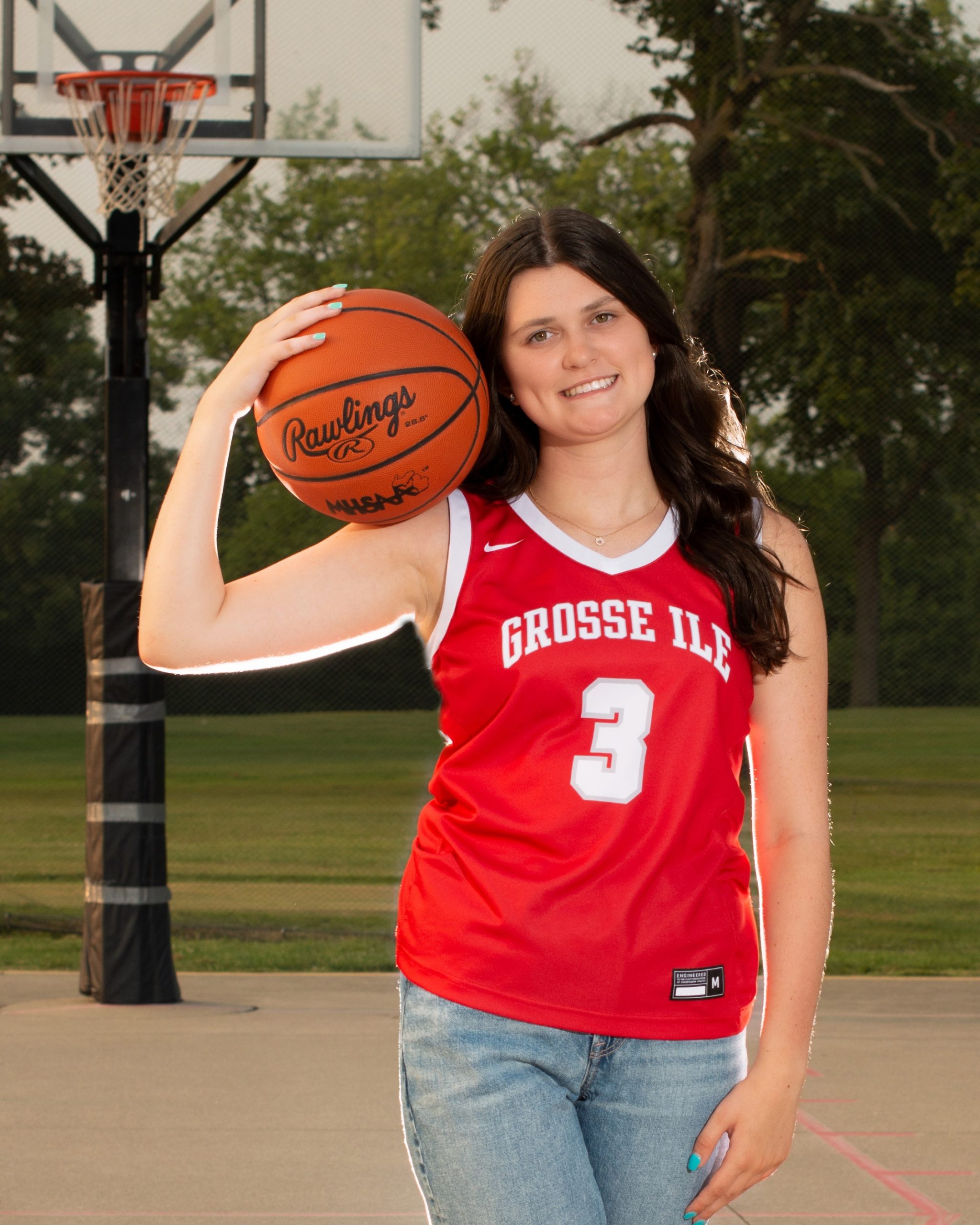 Grosse Ile student sitting on basketball court with ball, casual pose