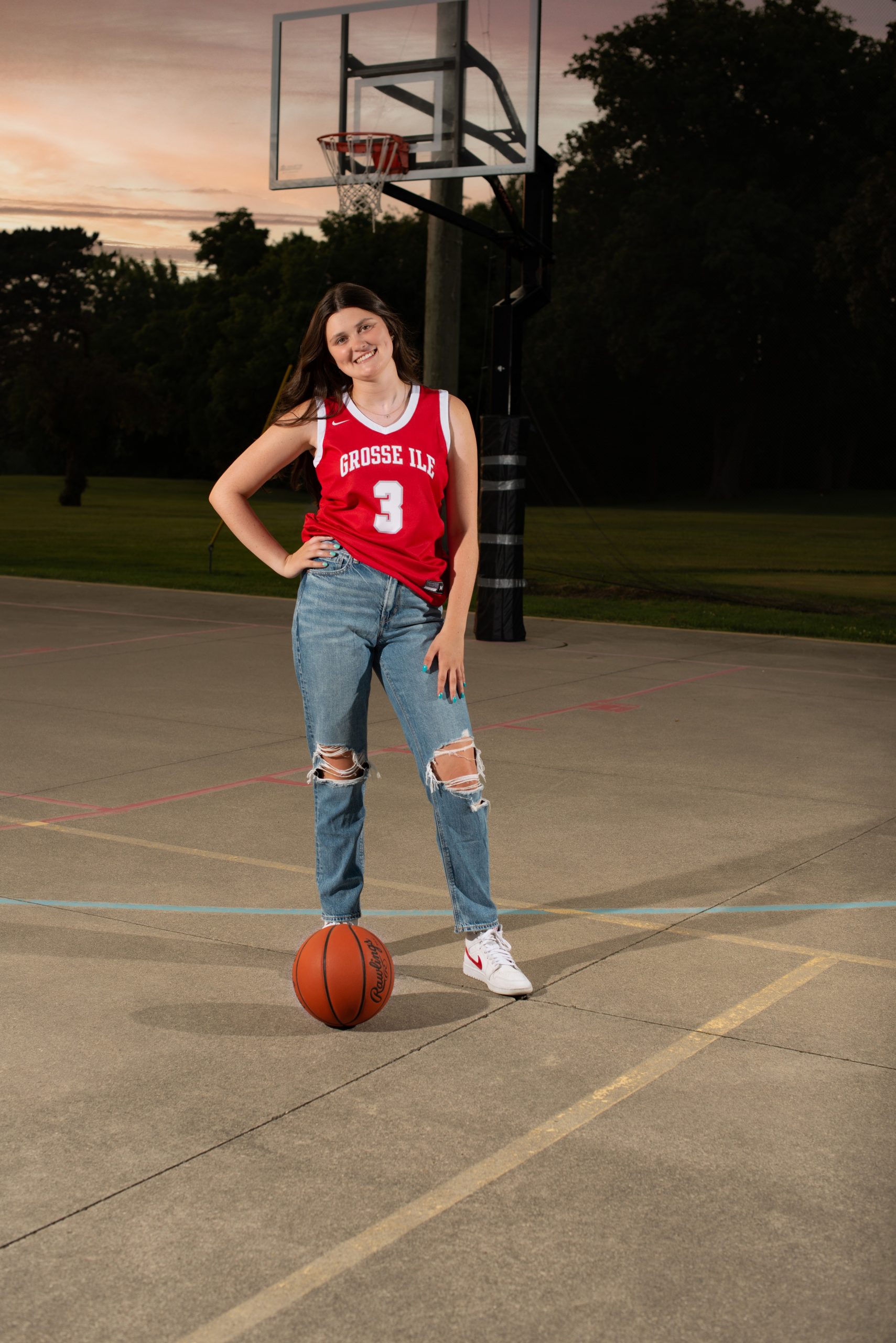 Grosse Ile student sitting on basketball court with ball, casual pose