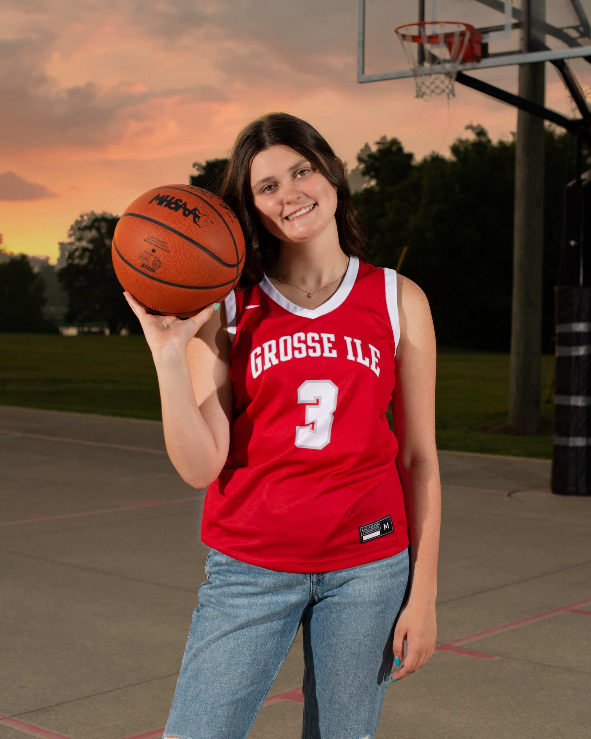 Grosse Ile student sitting on basketball court with ball, casual pose