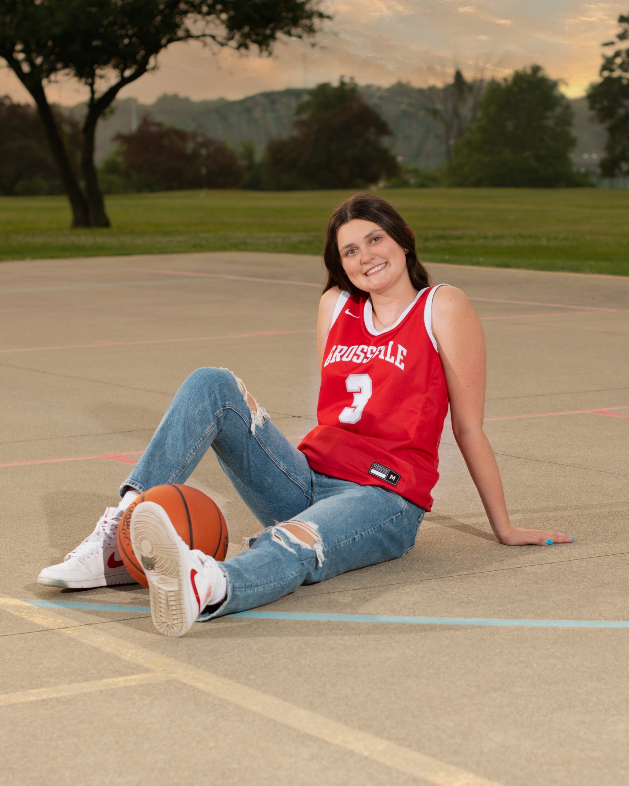 Grosse Ile student sitting on basketball court with ball, casual pose