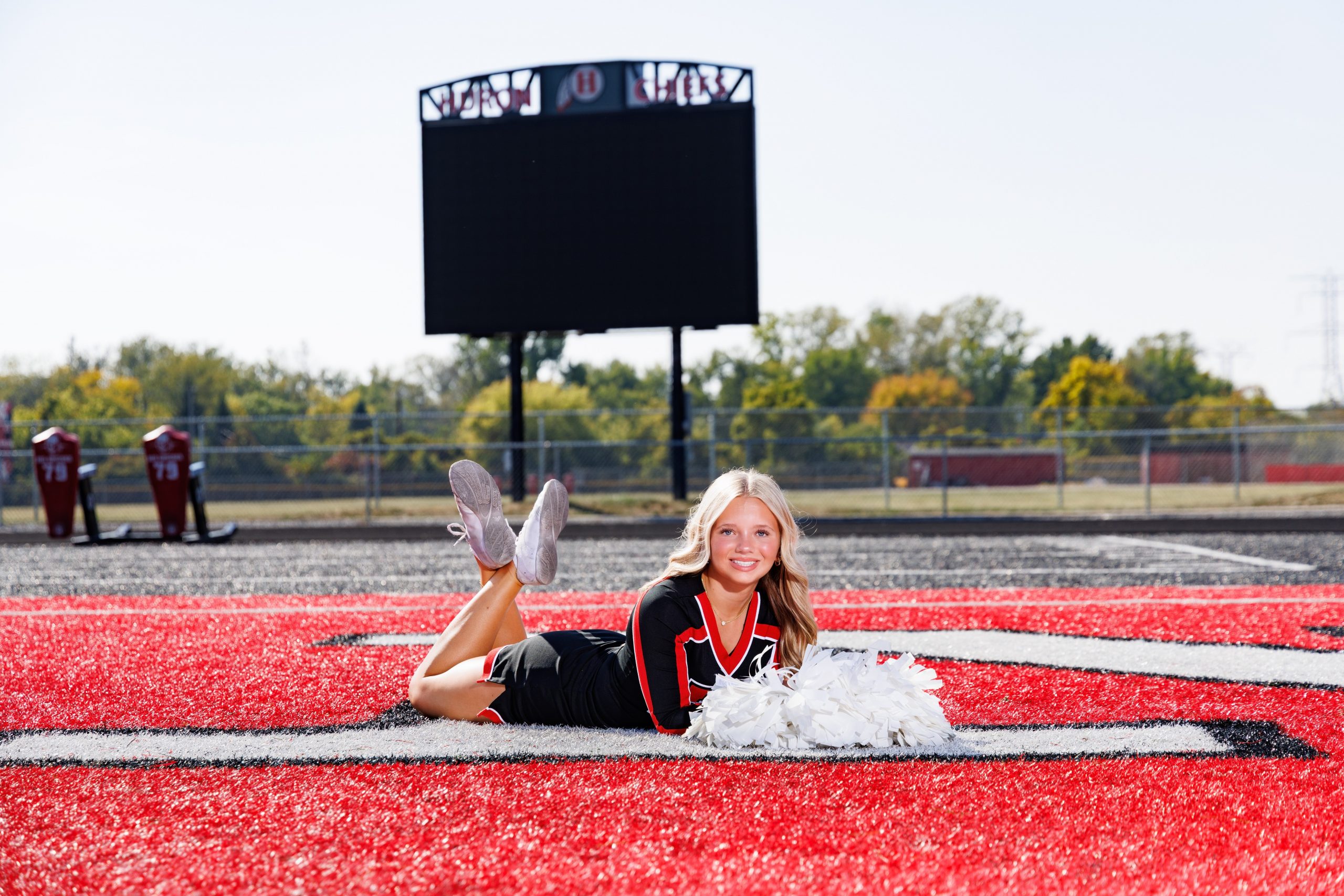 Huron cheer team member reclining on turf with silver and red pom-poms near scoreboard