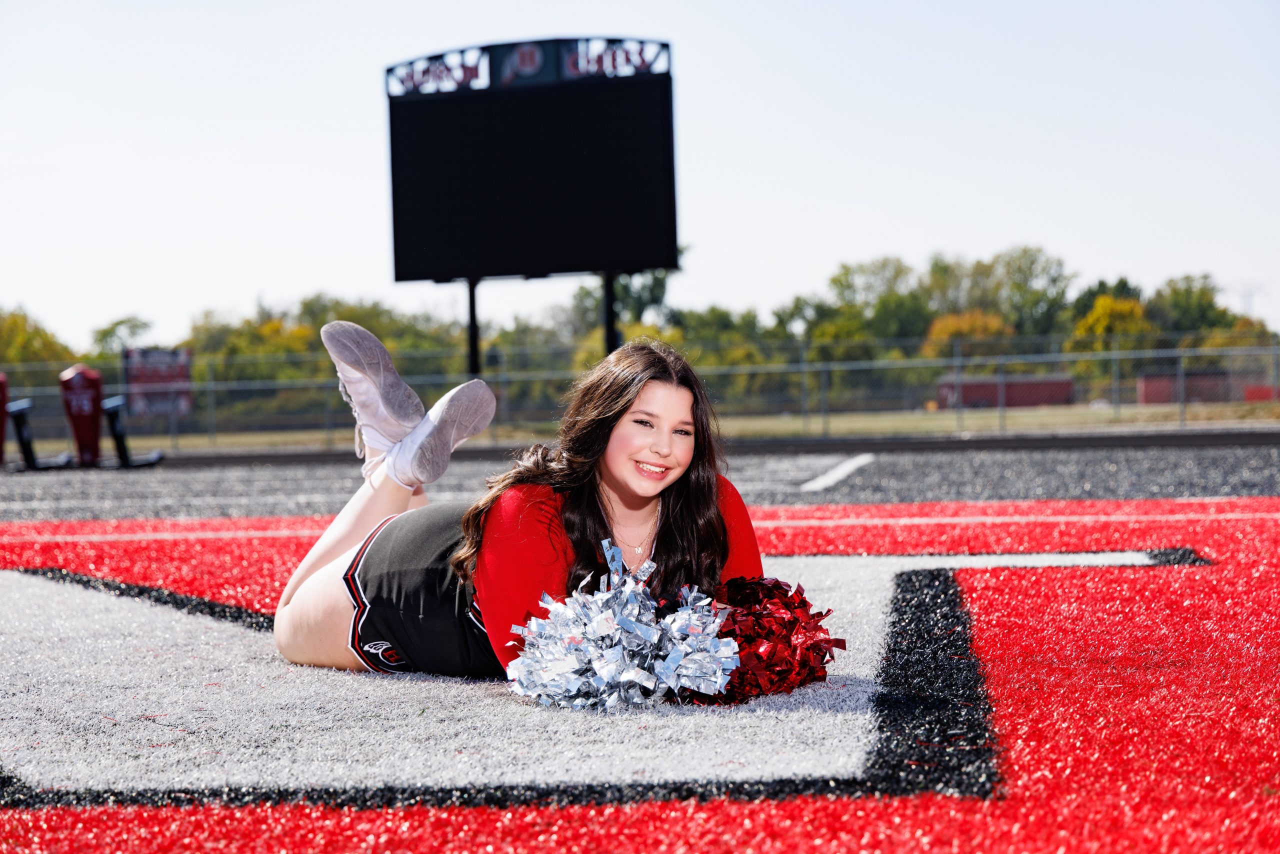 Cheerleader wearing Huron uniform seated on field holding red pom-poms
