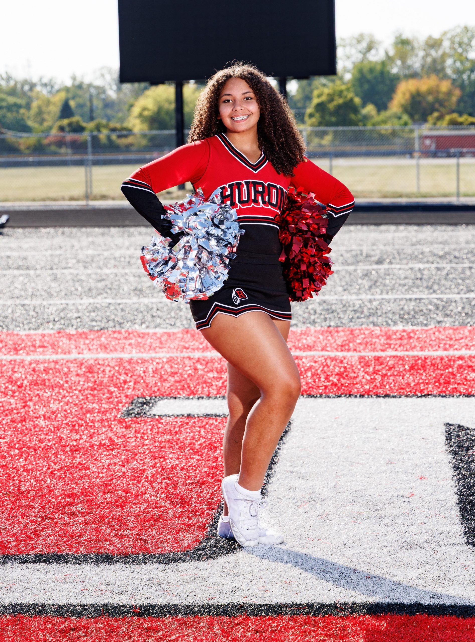 Huron cheer team photo featuring white pom-poms and athletic field backdrop