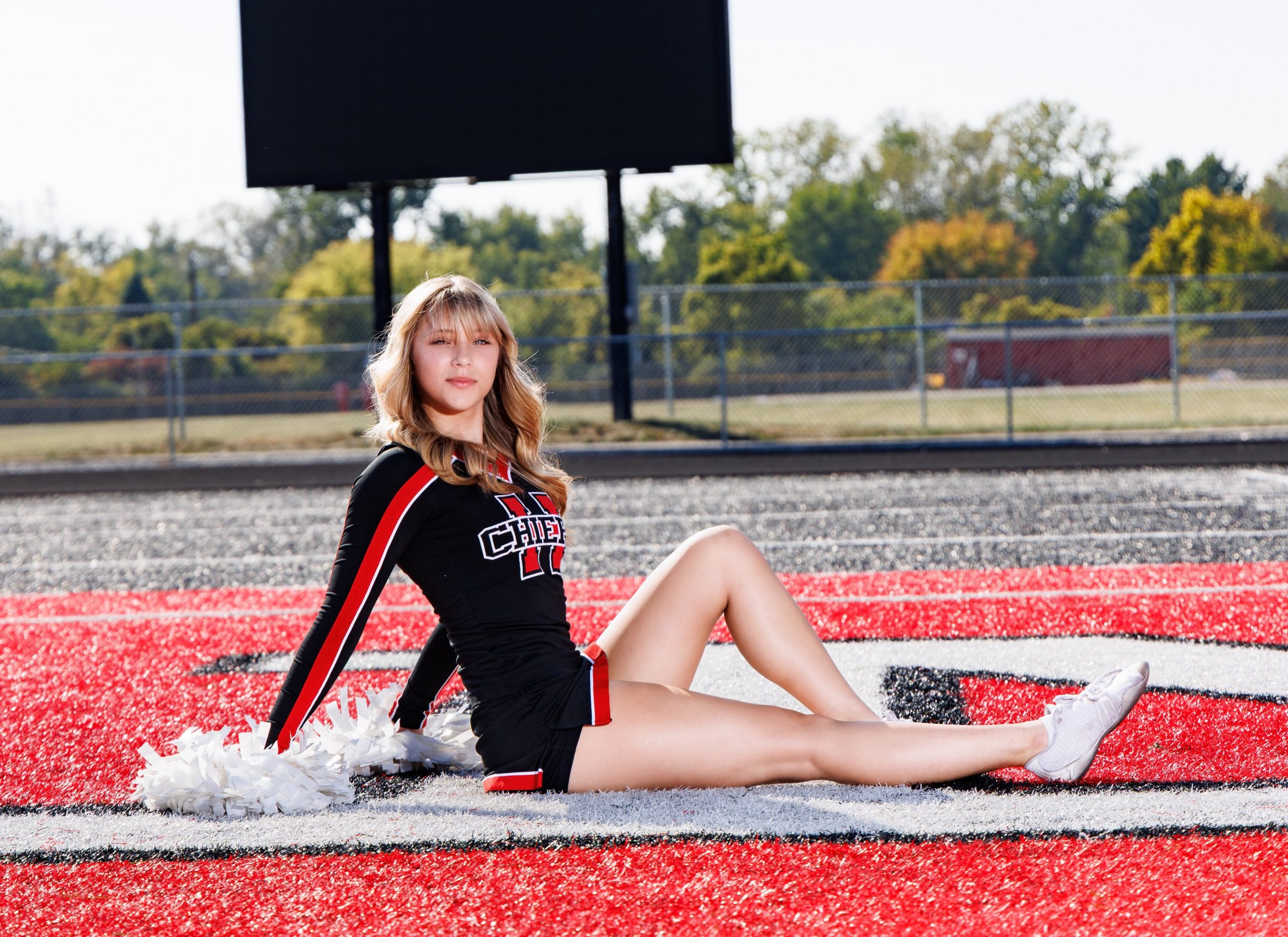 Huron cheer team photo featuring white pom-poms and athletic field backdrop