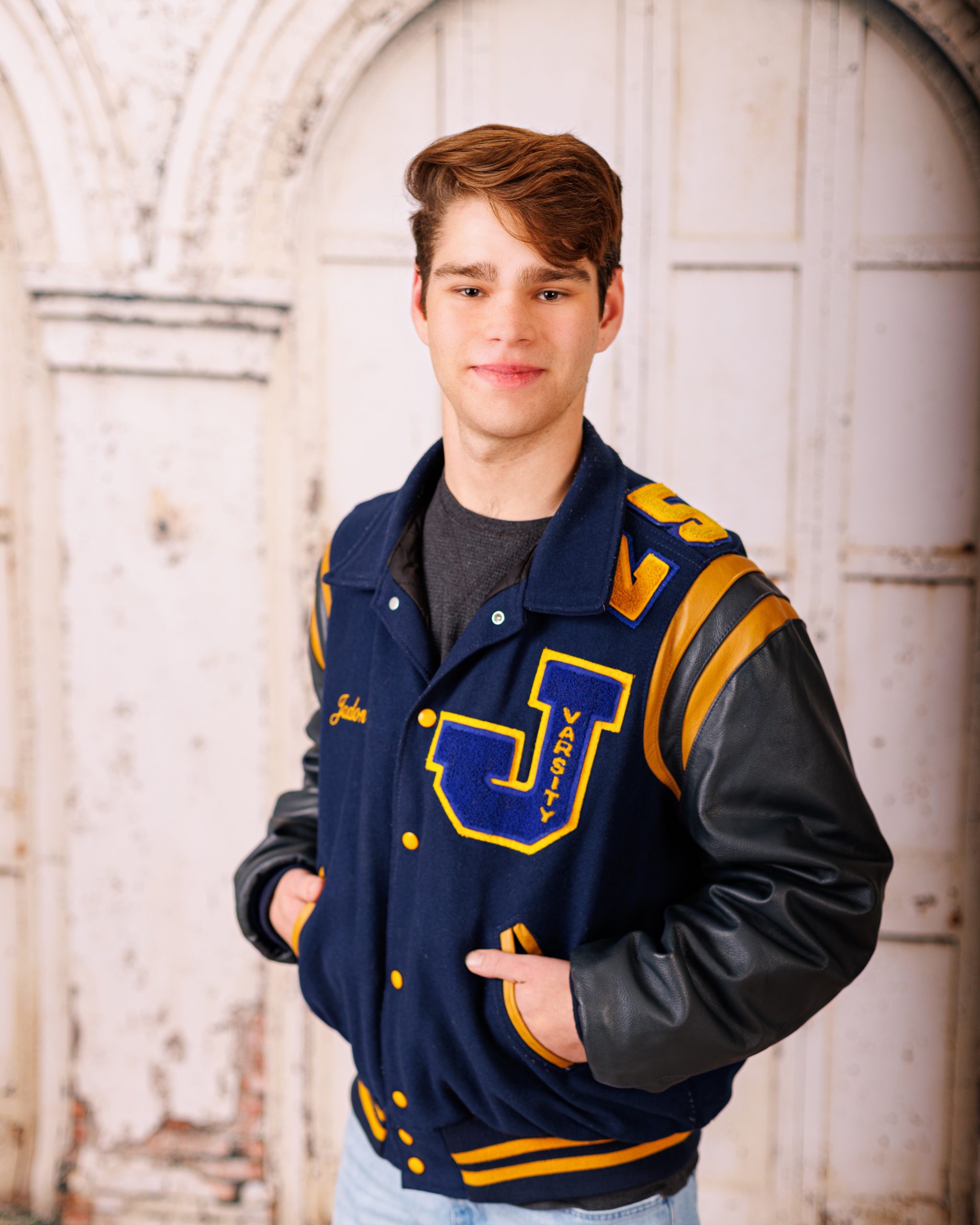 Graduate in a navy cap and gown with a blue and gold tassel, smiling for his senior portrait.