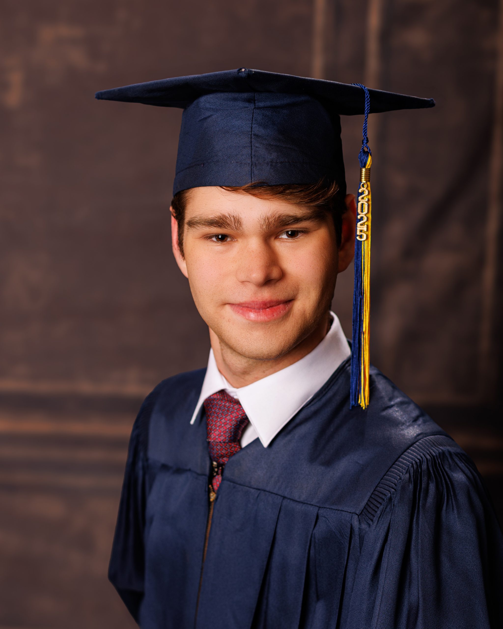 Stylishly dressed young man in a navy three-piece suit posing confidently against a dark backdrop.