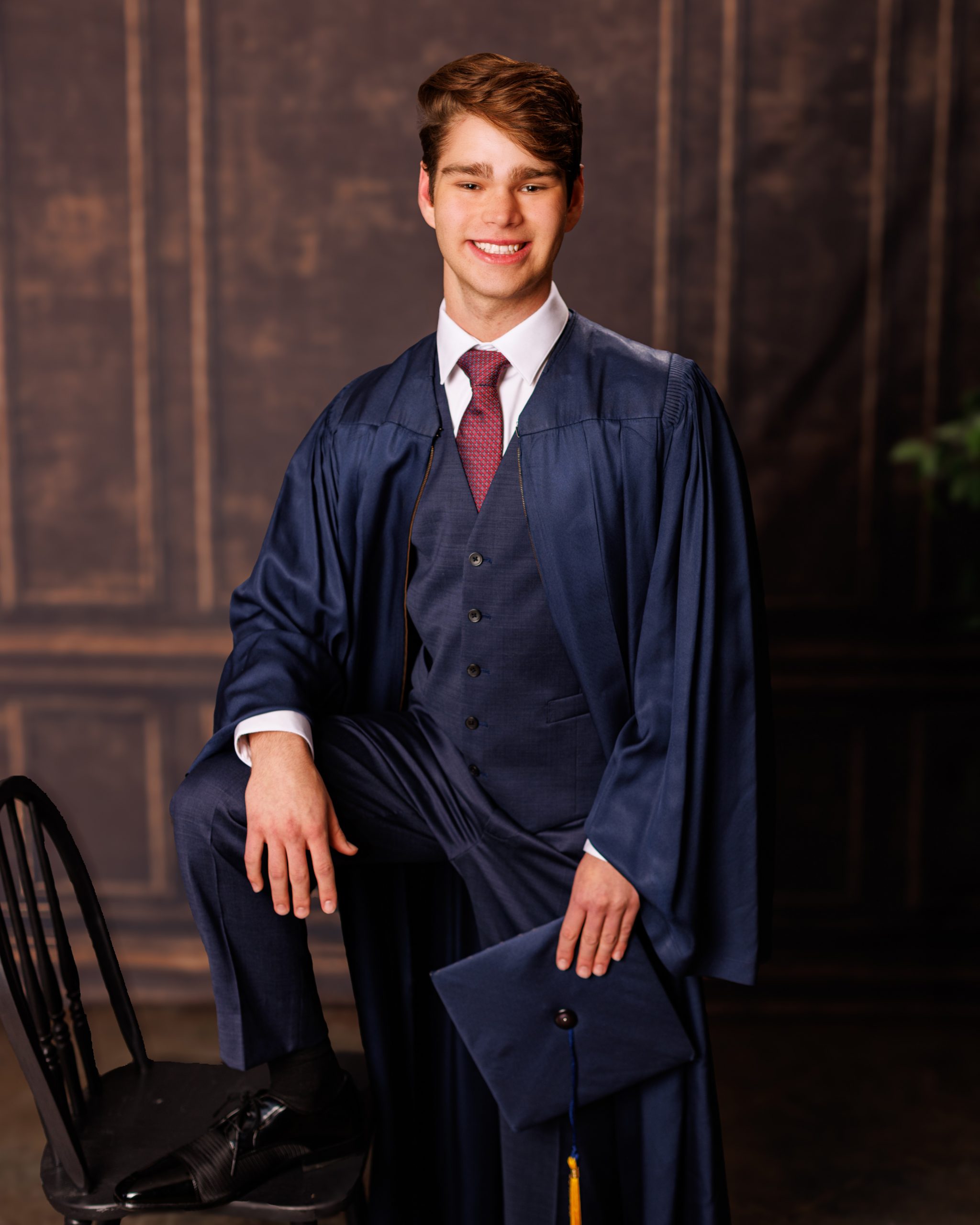 Stylishly dressed young man in a navy three-piece suit posing confidently against a dark backdrop.