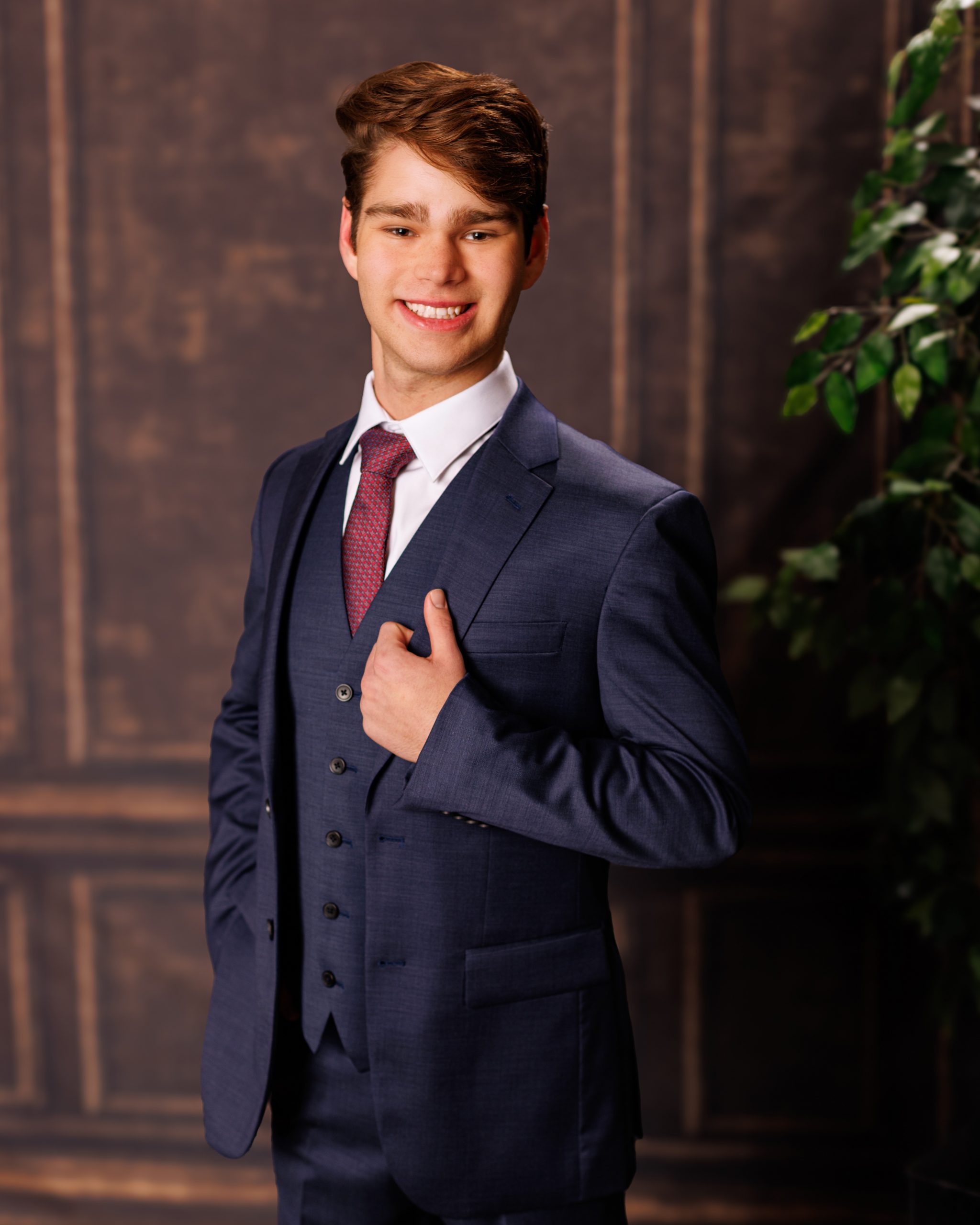 Stylishly dressed young man in a navy three-piece suit posing confidently against a dark backdrop.