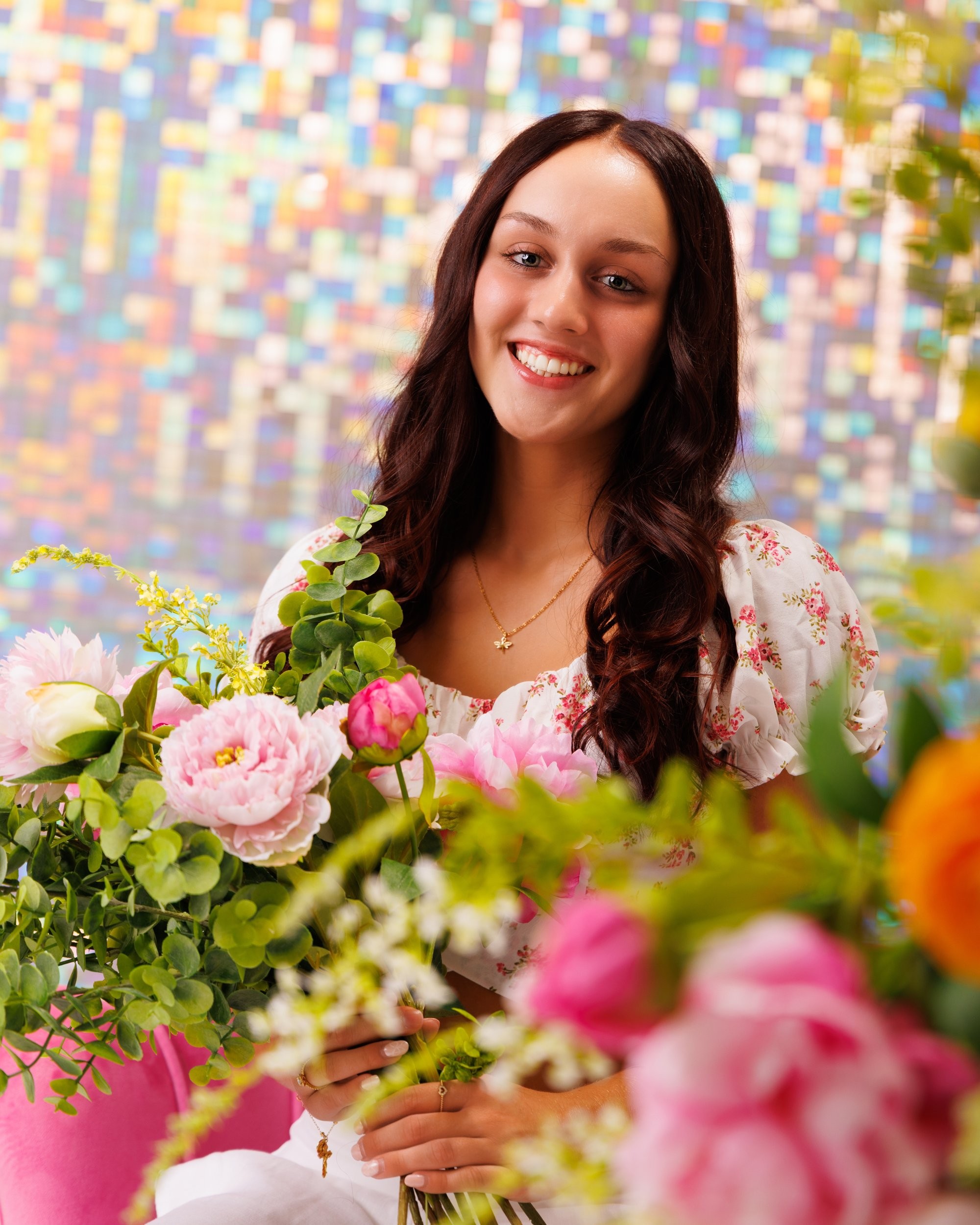 Kourtney's senior portrait with lush floral arrangements against a vibrant studio setting