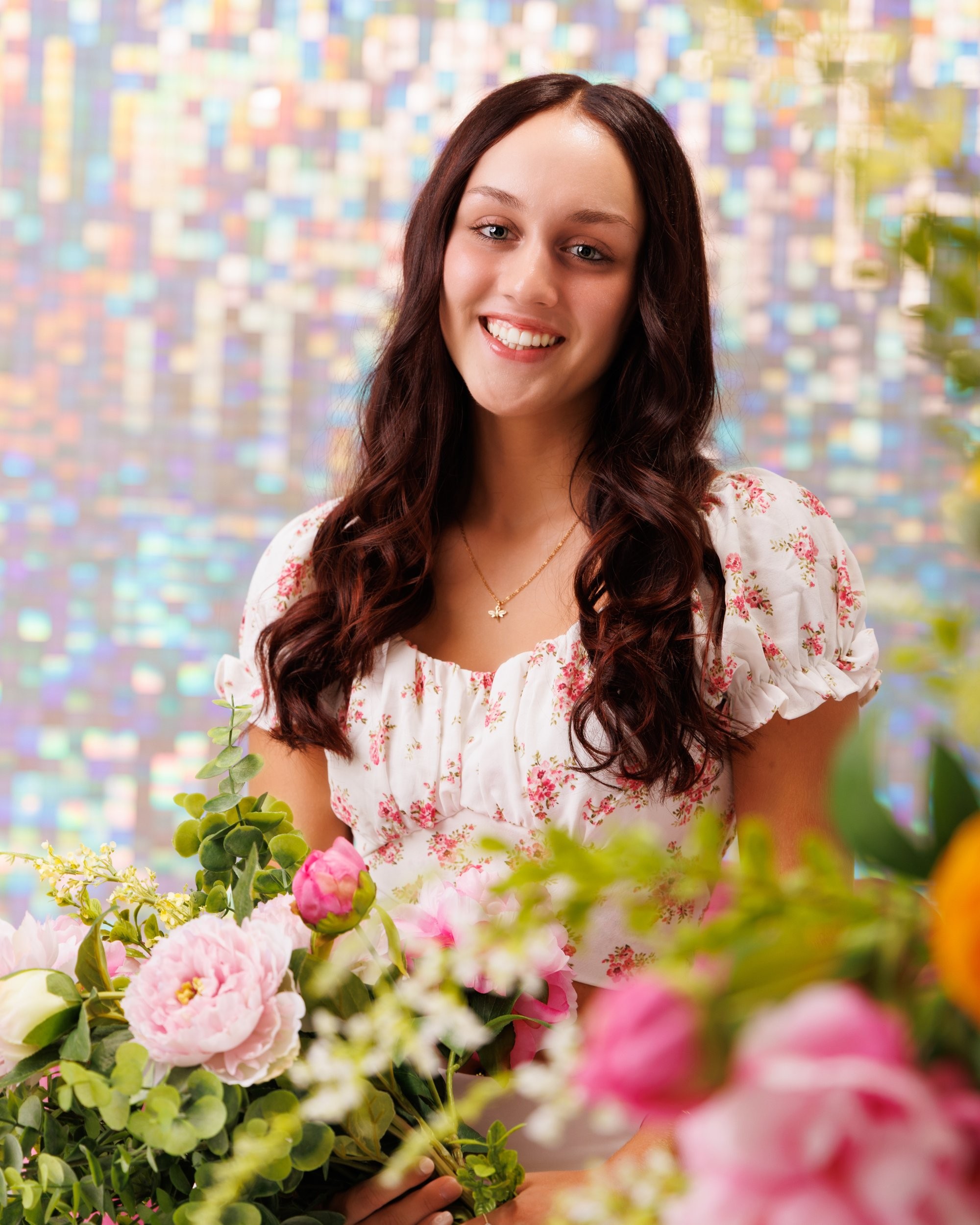 Kourtney's senior portrait with lush floral arrangements against a vibrant studio setting