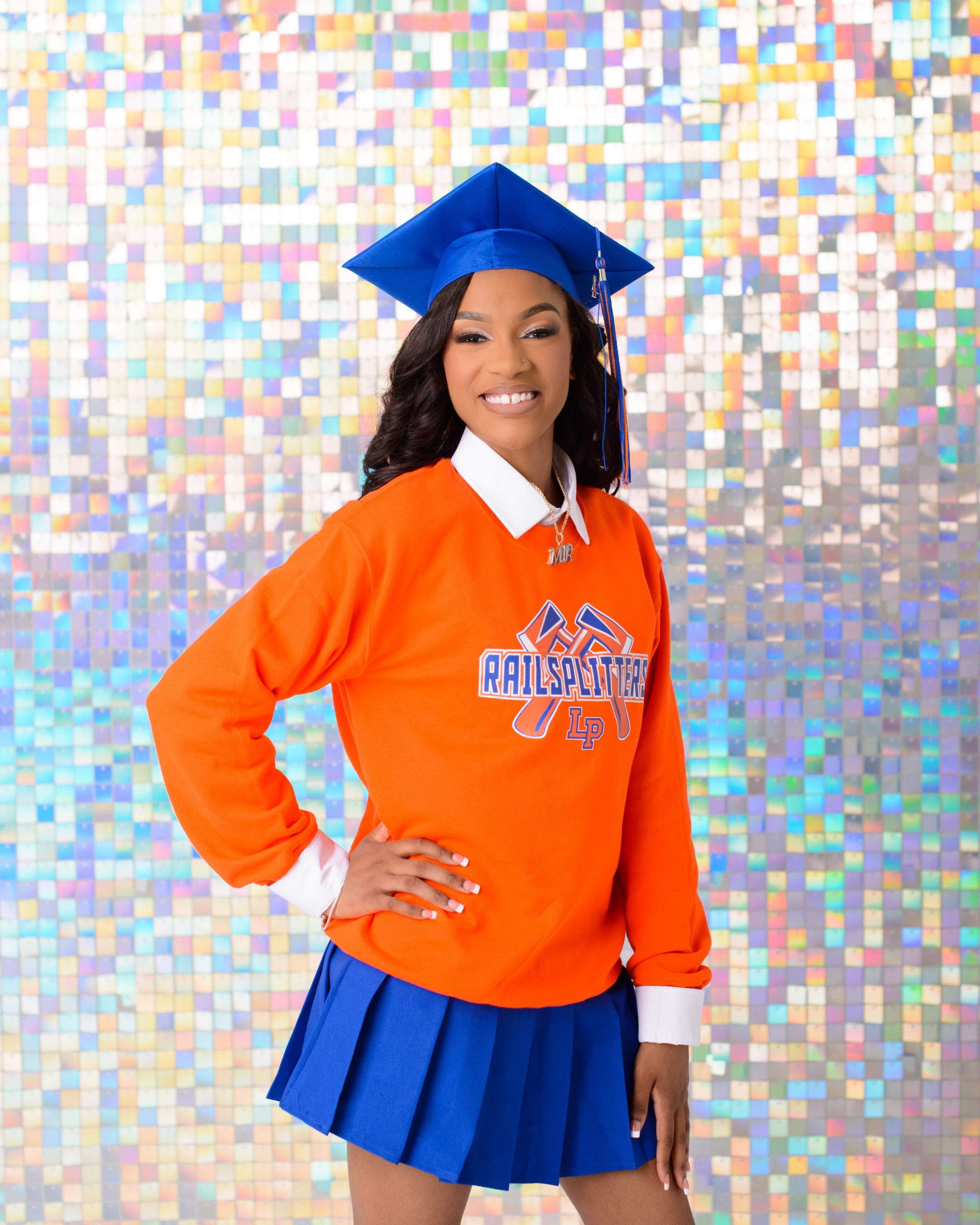 Senior girl wearing blue graduation cap and orange Rail Splitters sweatshirt posing against a mosaic background
