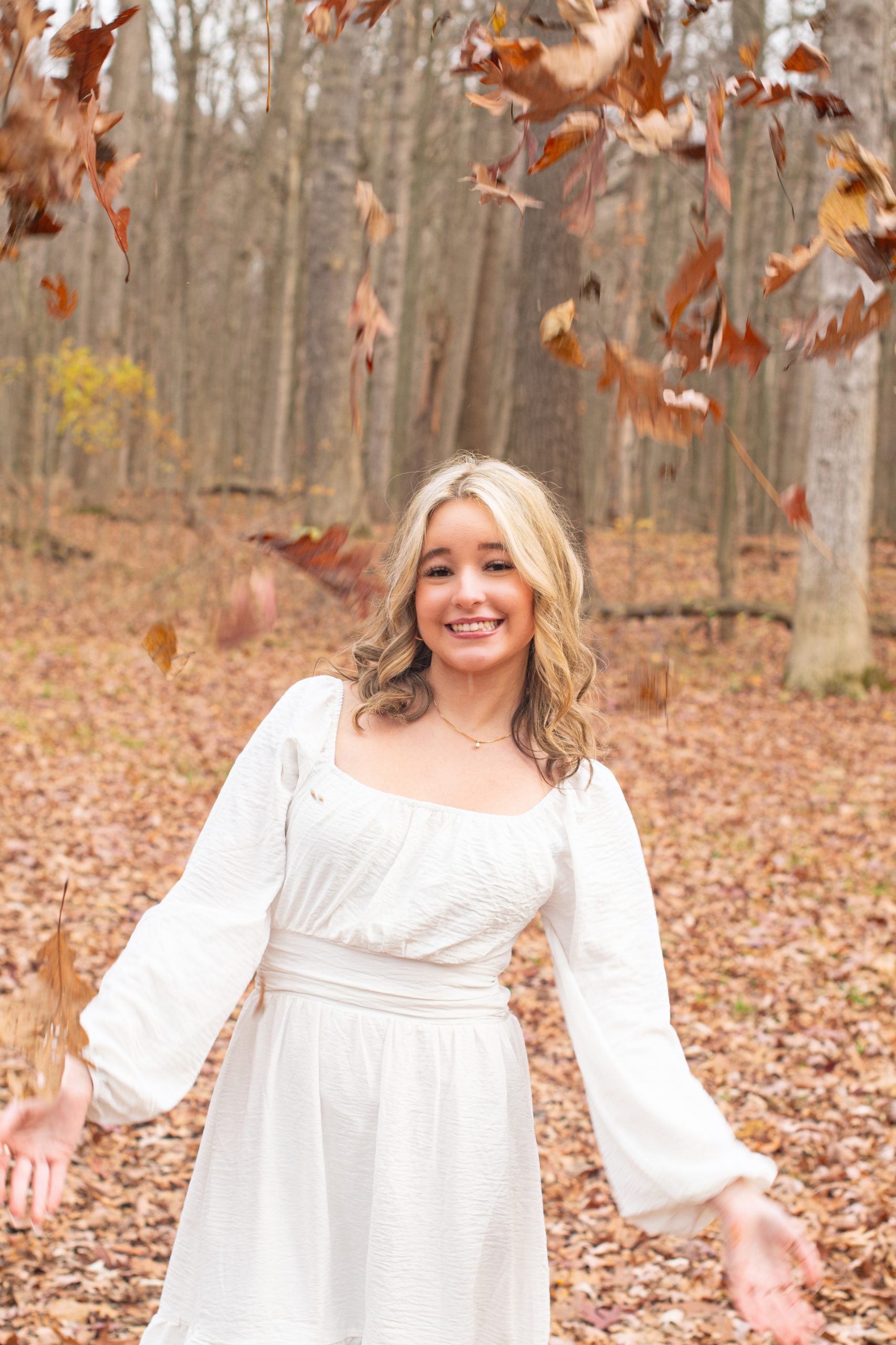senior girl lying on autumn leaves in a forest setting, dressed in cozy sweater and jeans