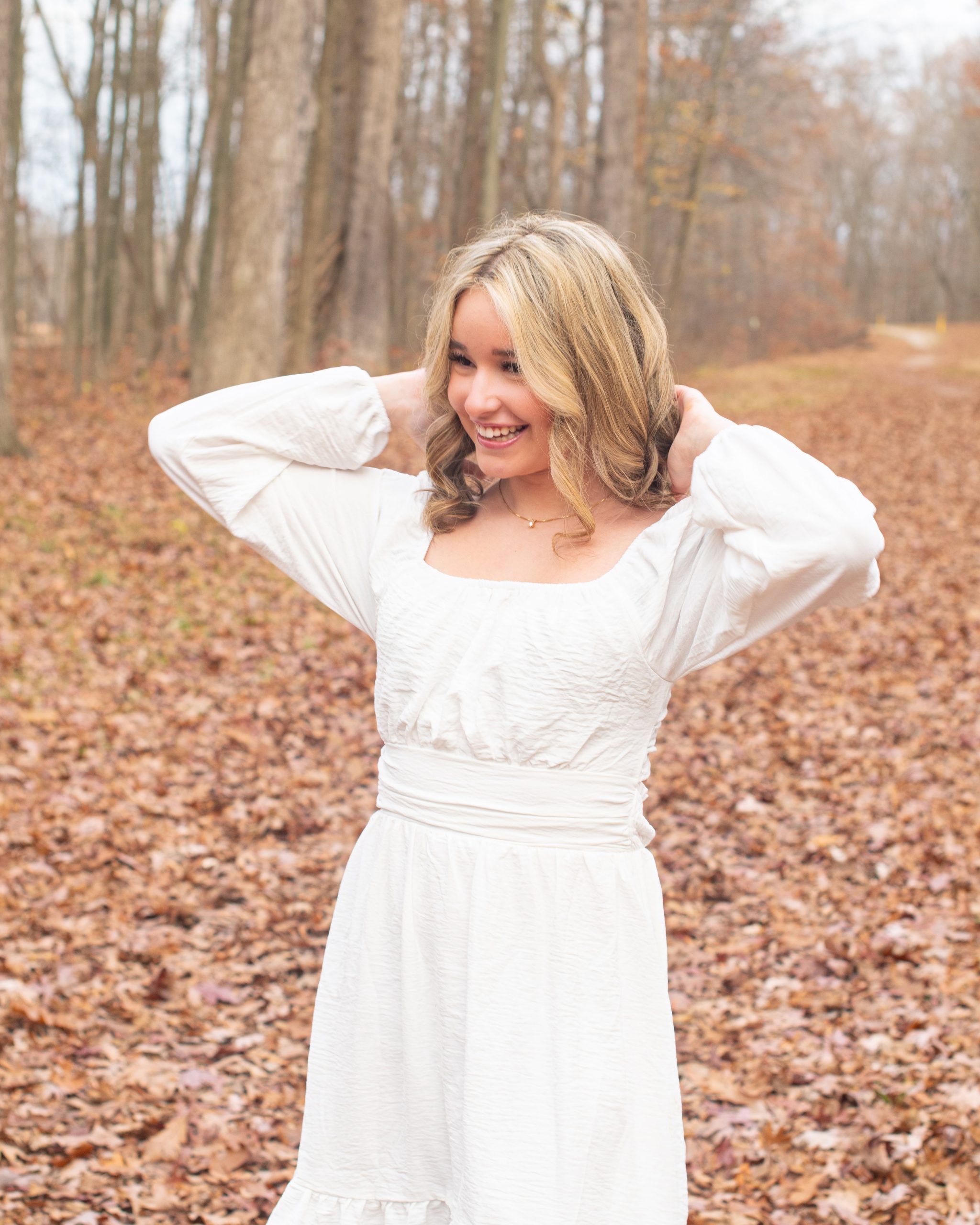 senior girl lying on autumn leaves in a forest setting, dressed in cozy sweater and jeans