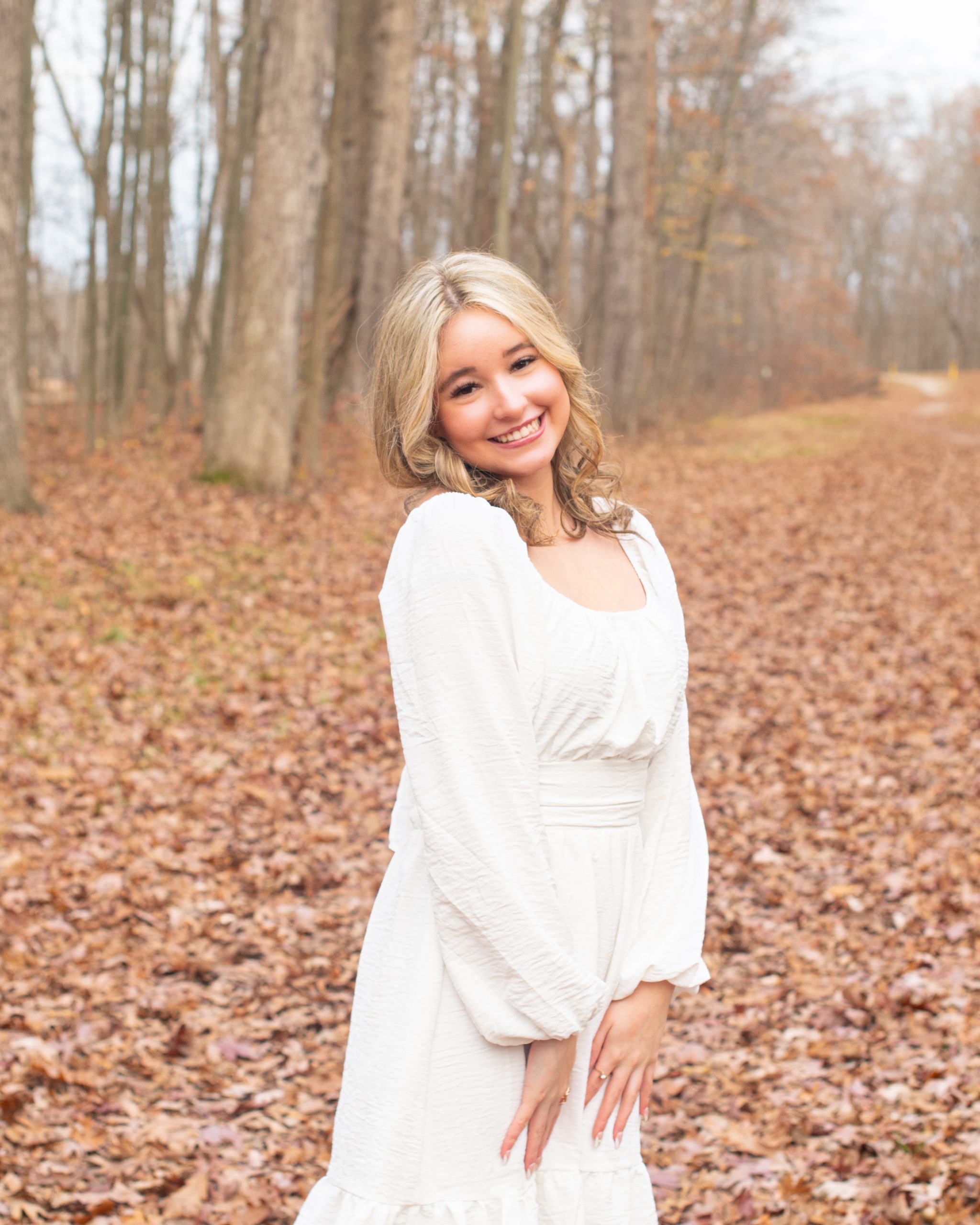 senior girl lying on autumn leaves in a forest setting, dressed in cozy sweater and jeans