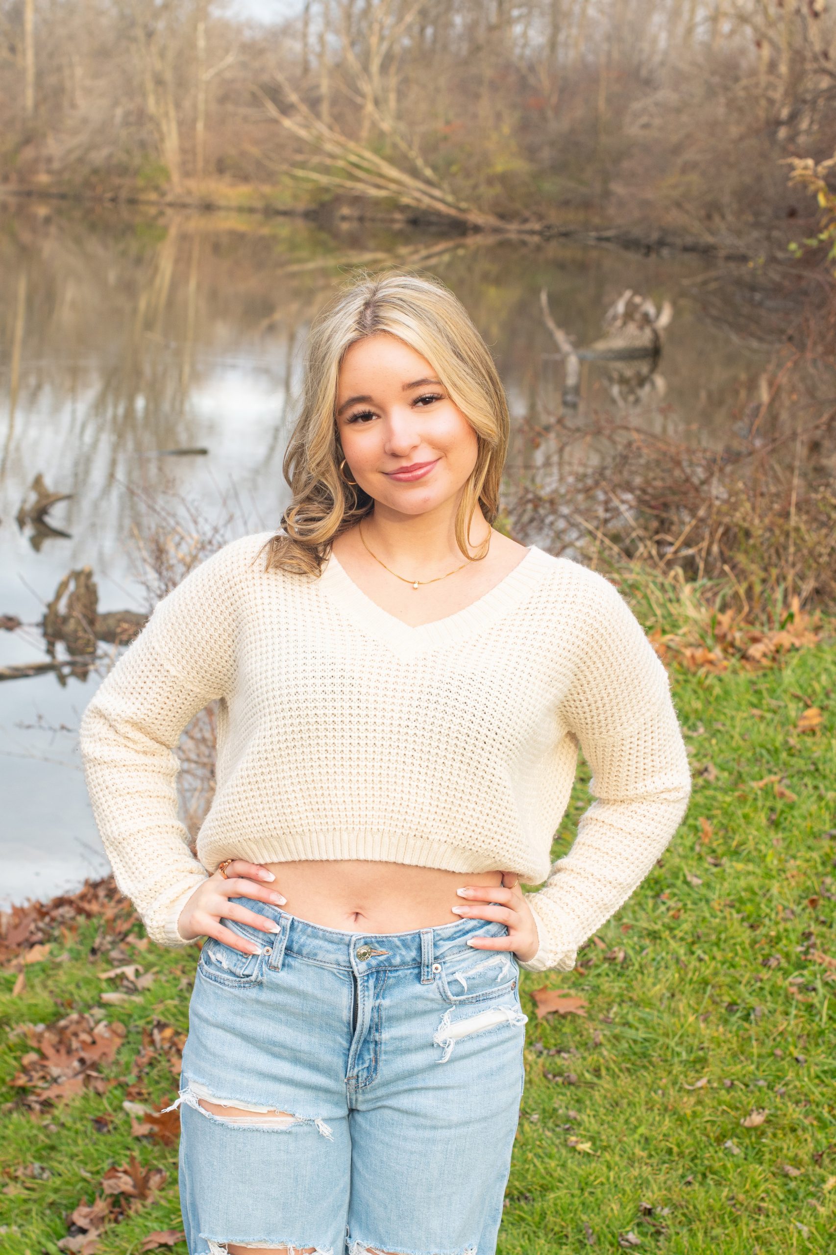 senior girl lying on autumn leaves in a forest setting, dressed in cozy sweater and jeans