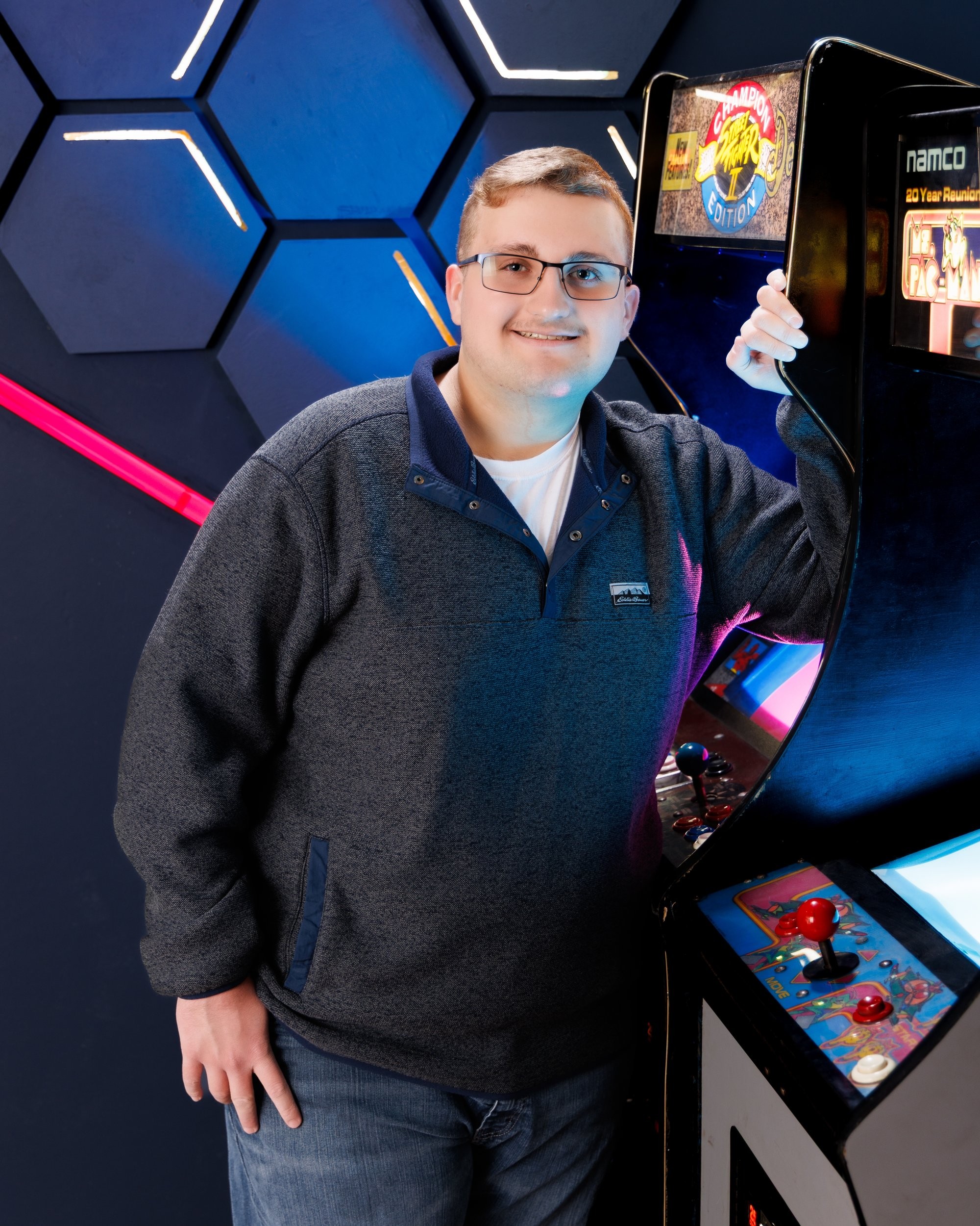 Aiden holding a 'Street Fighter' arcade cabinet in a colorful photo session