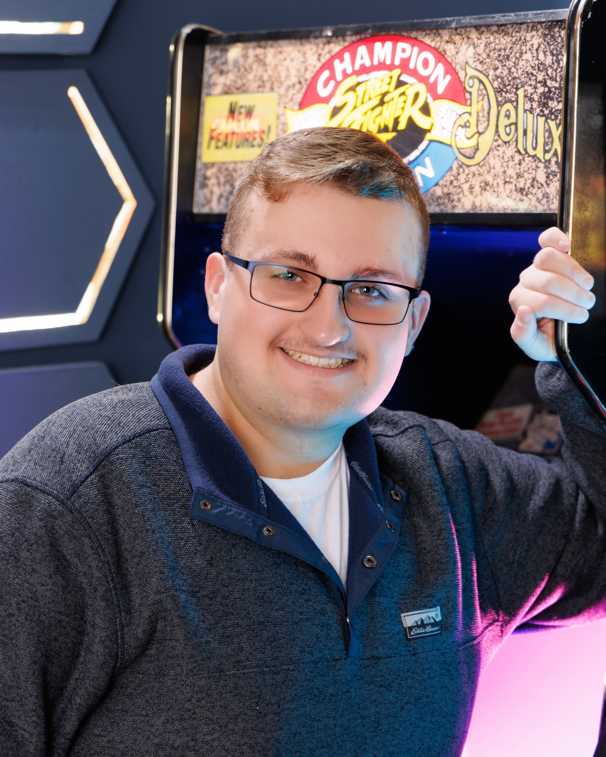 Aiden holding a 'Street Fighter' arcade cabinet in a colorful photo session