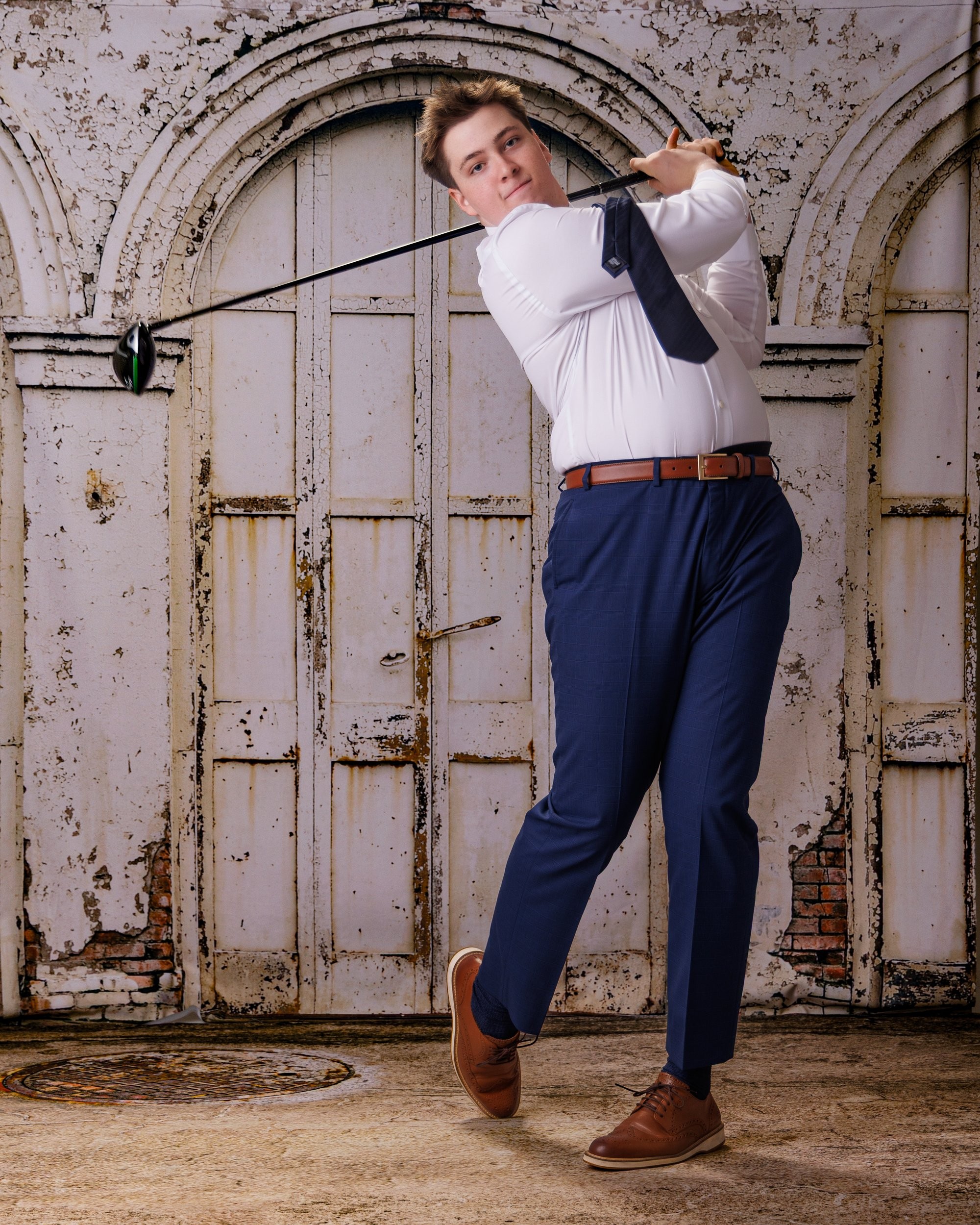 Senior portrait of young man holding golf club, dressed formally, standing confidently before aged architectural backdrop