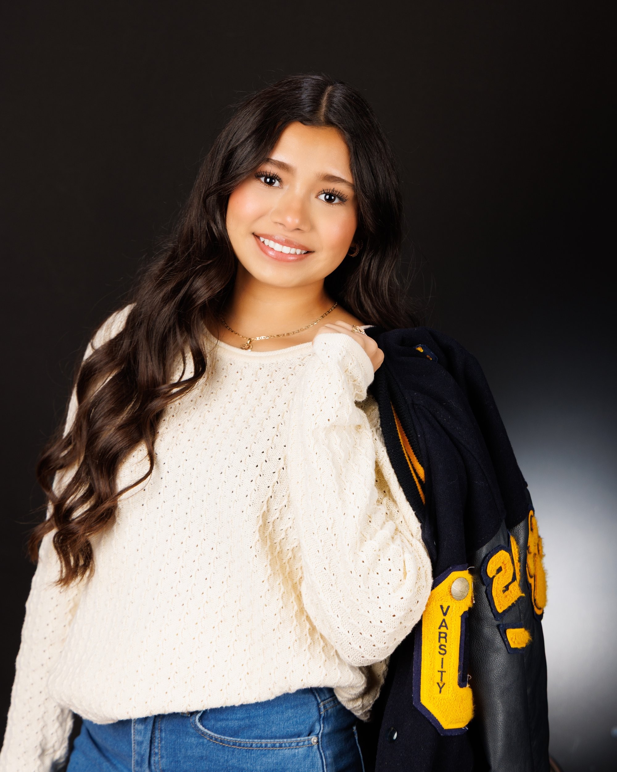 Maria in cream sweater with varsity jacket draped over shoulder