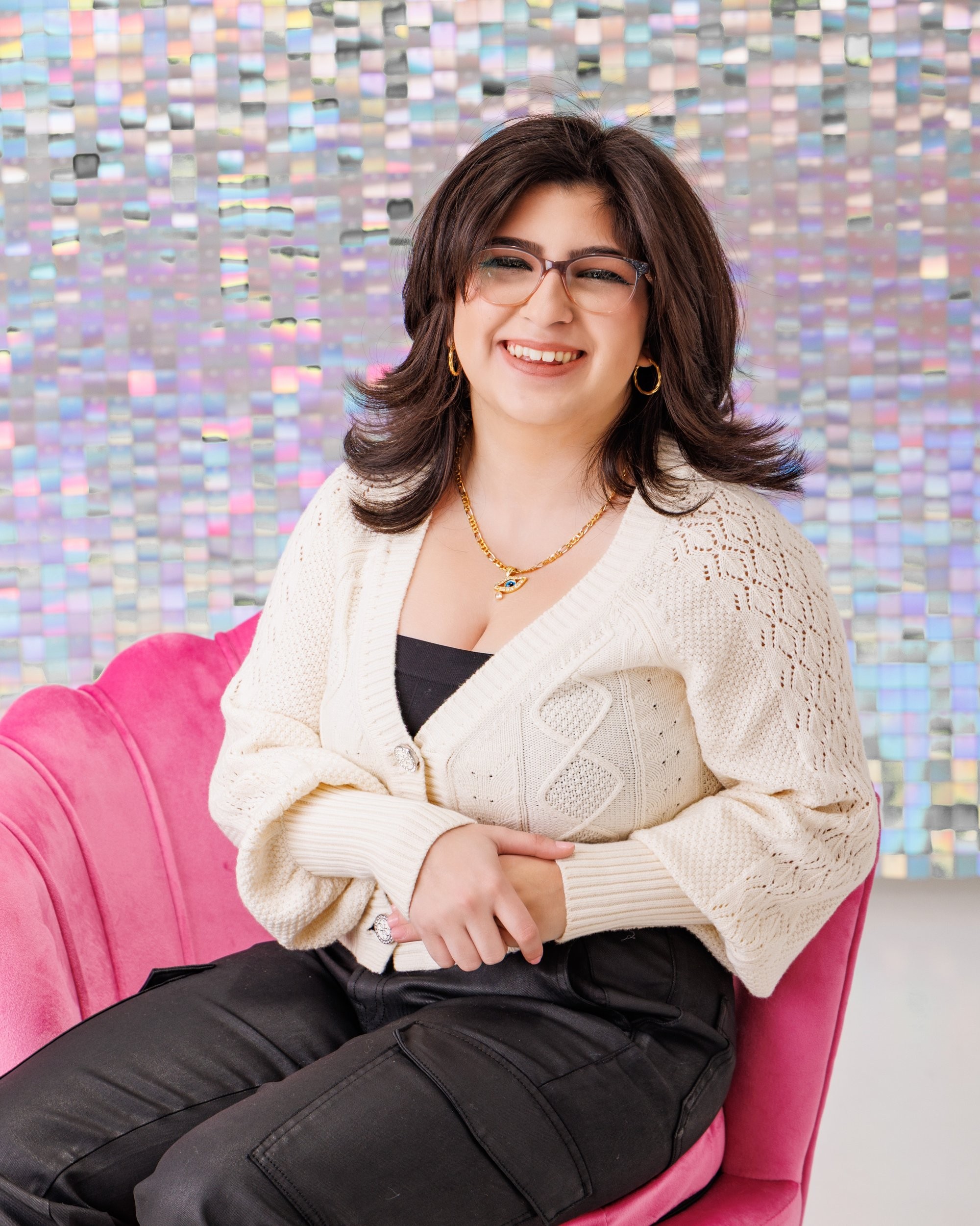 Seated senior portrait with iridescent tile wall and pink couch backdrop