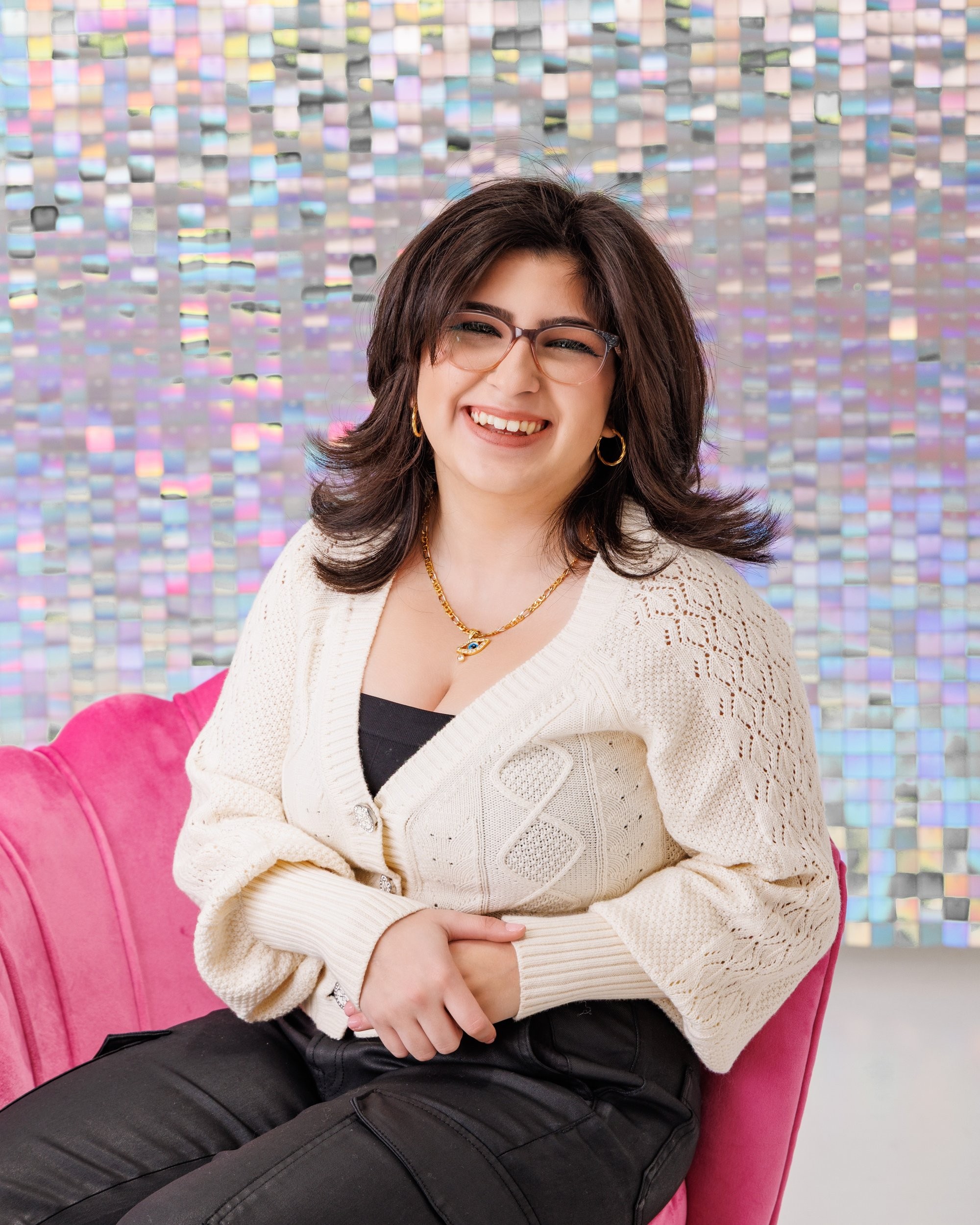 Seated senior portrait with iridescent tile wall and pink couch backdrop