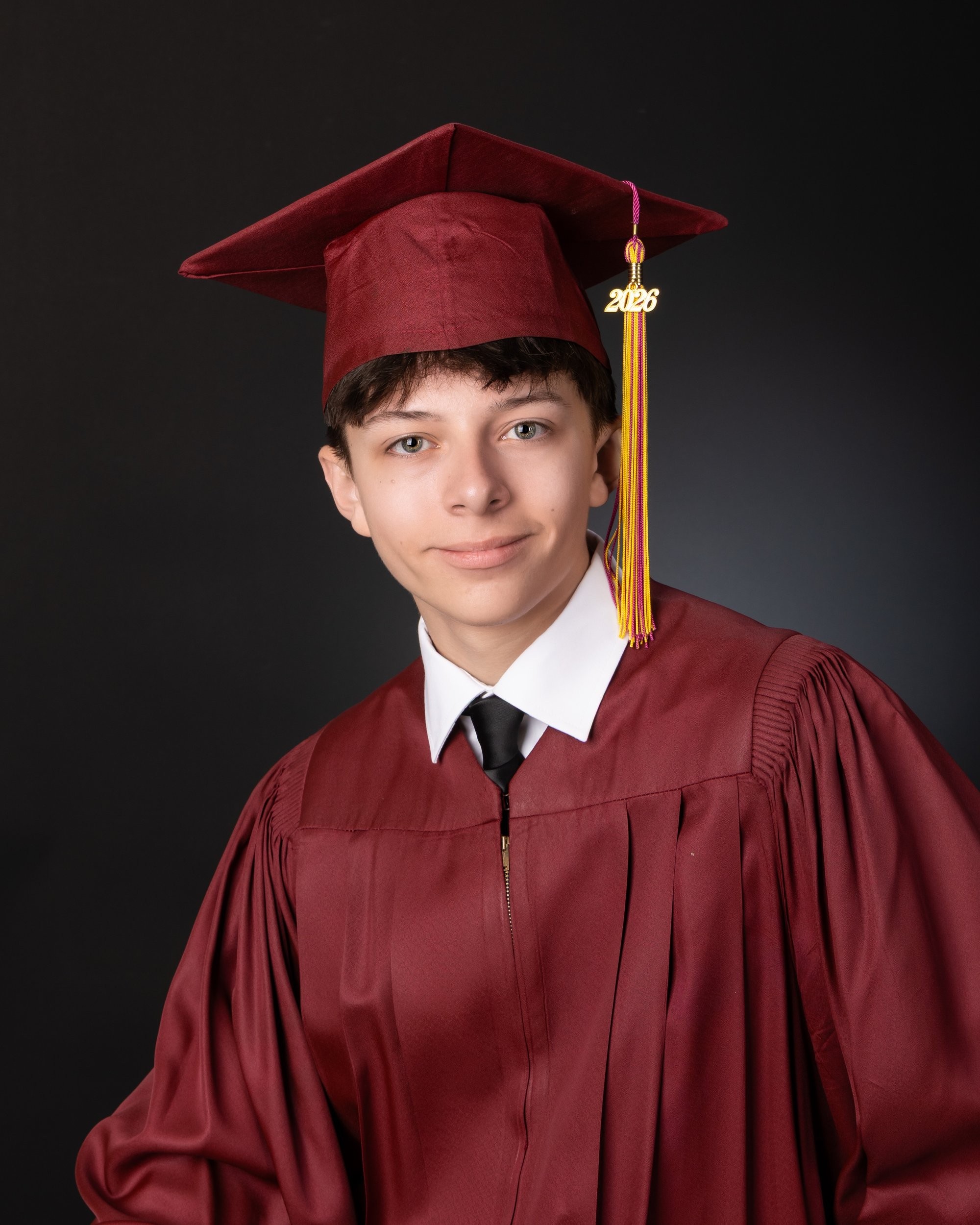 Casual senior photograph featuring a young man in a black polo shirt seated with books behind him, set in a dimly lit room