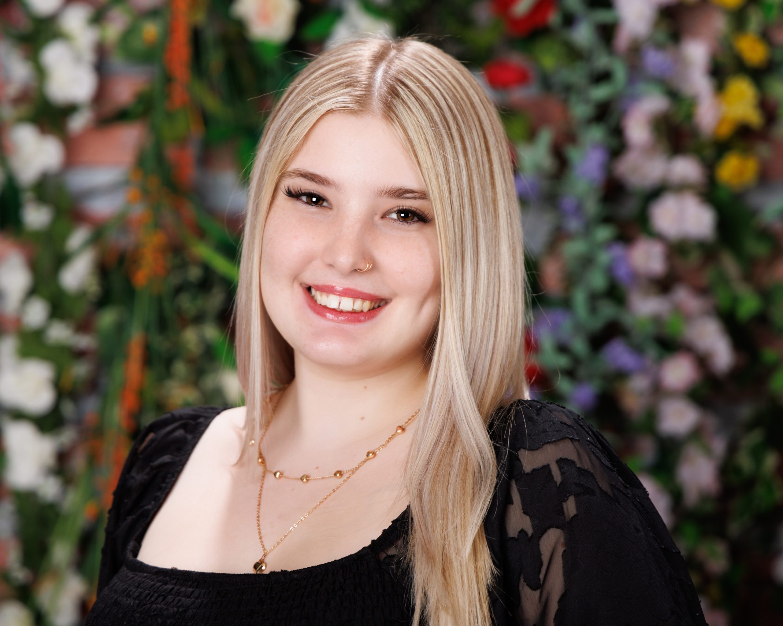 Alysha wearing black lace dress with floral backdrop for senior photography session