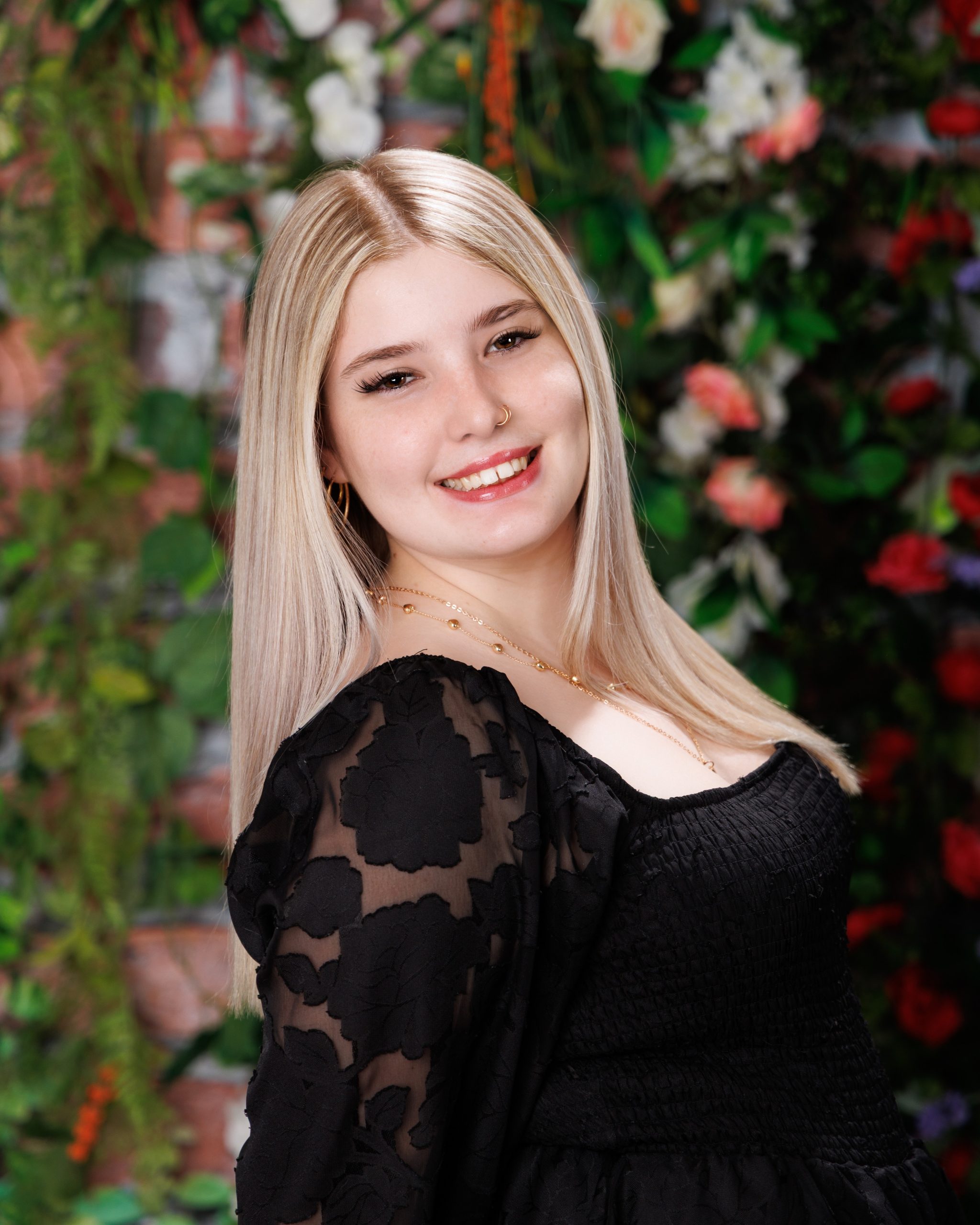 Alysha in black square-necked dress against floral background during senior portrait shoot