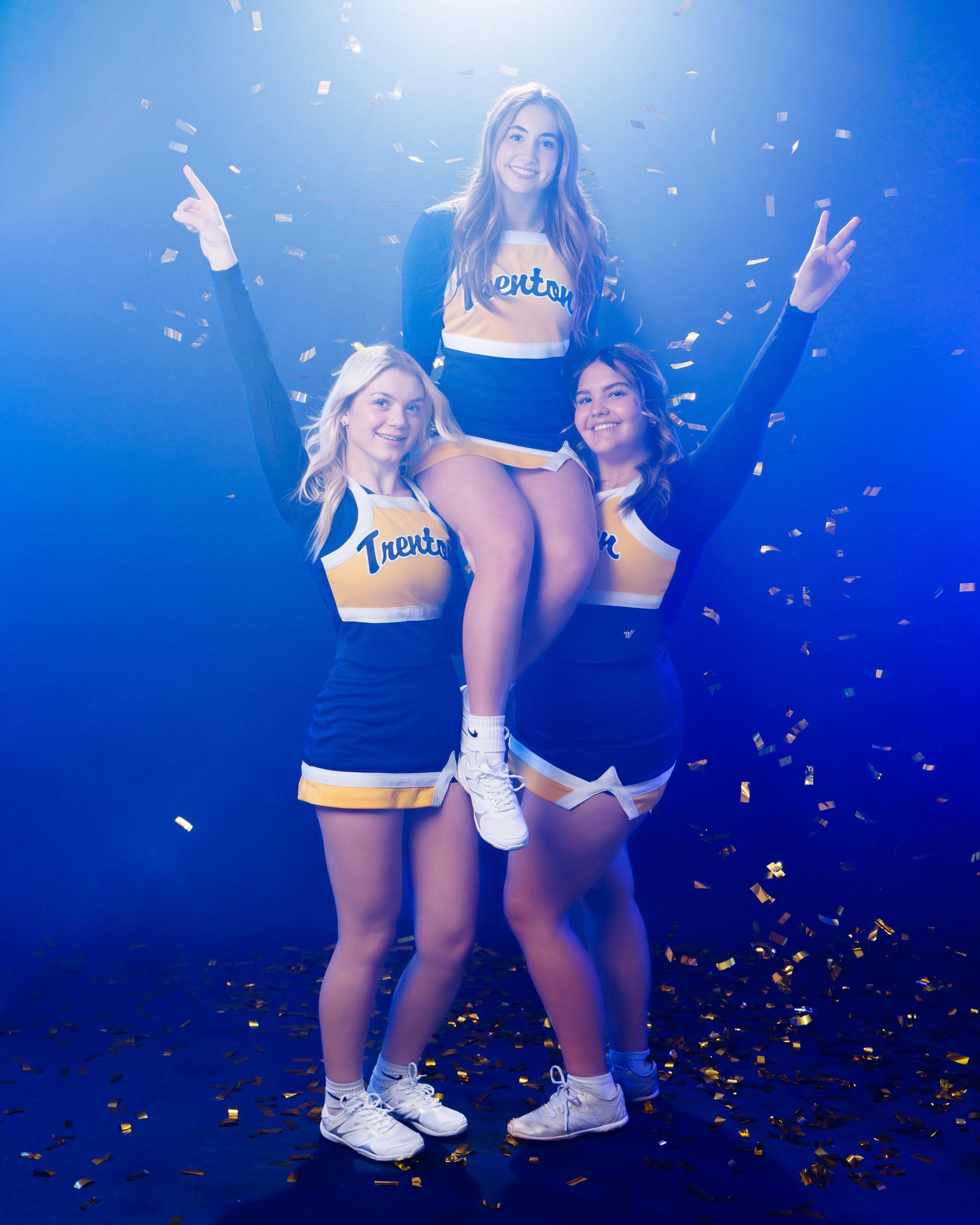 Cheerleader lying on floor in blue and gold uniform surrounded by confetti