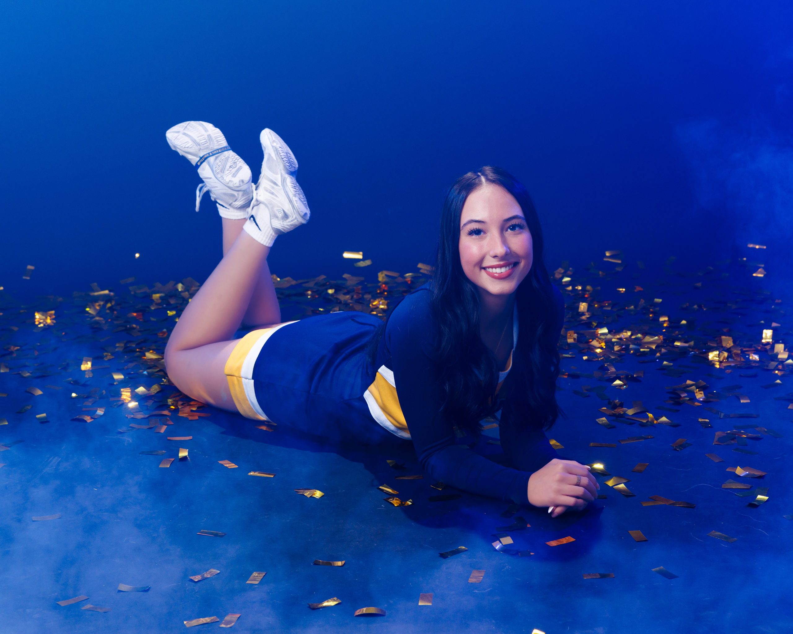 Cheerleader posing with hand on hip against blue backdrop with confetti