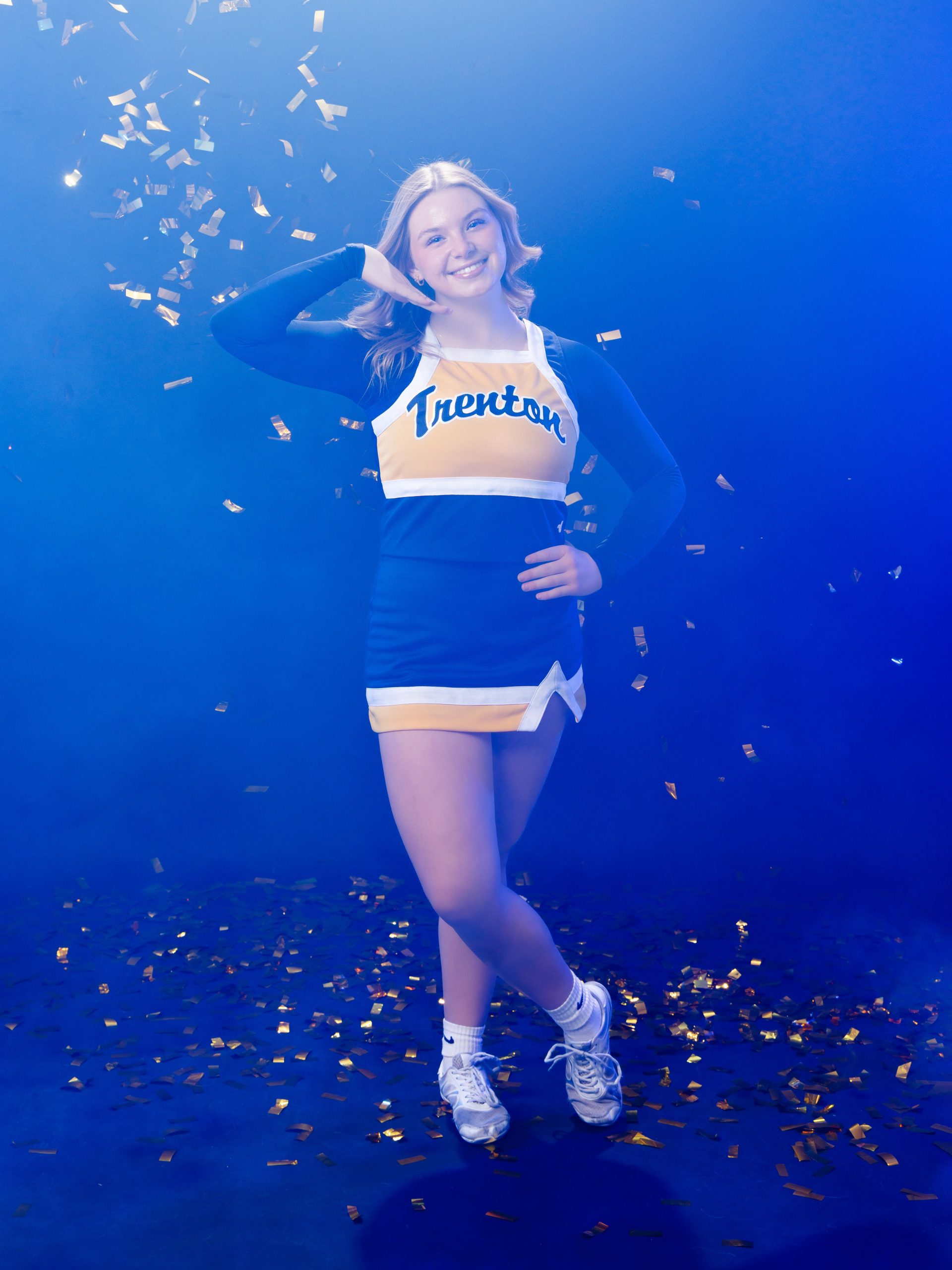 Cheerleader posing with hand on hip against blue backdrop with confetti