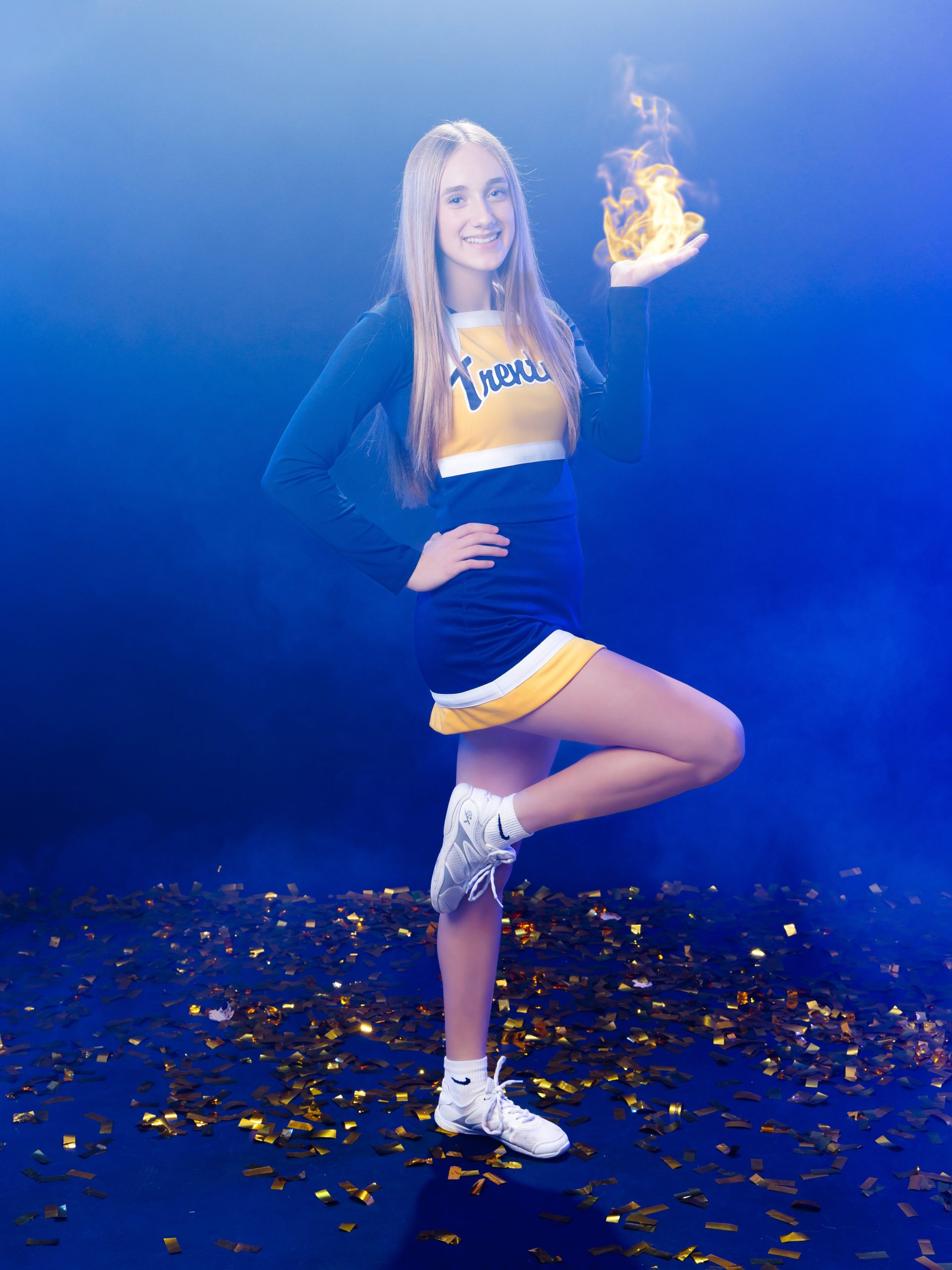 Cheerleader posing with hand on hip against blue backdrop with confetti