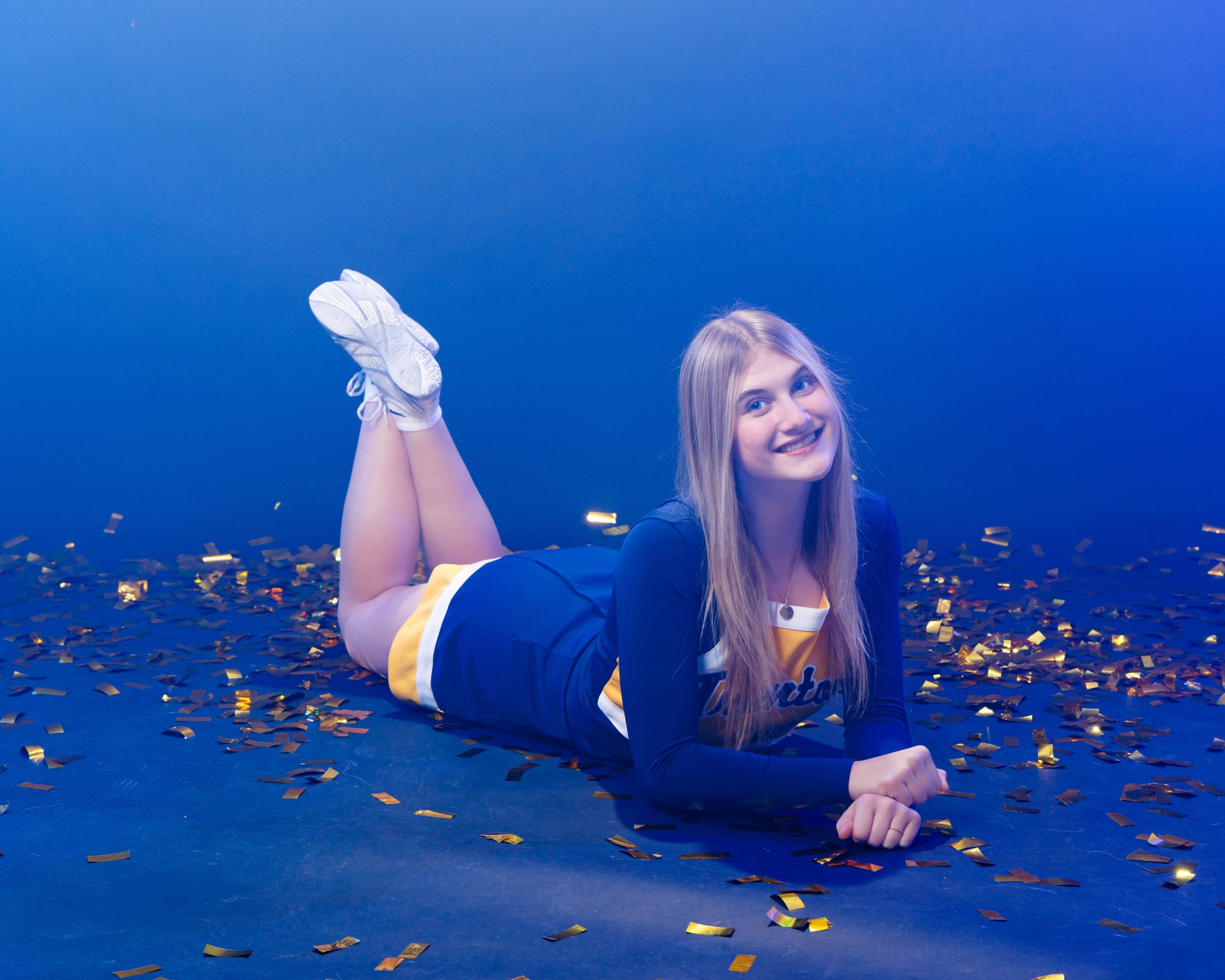 Cheerleader posing with hand on hip against blue backdrop with confetti