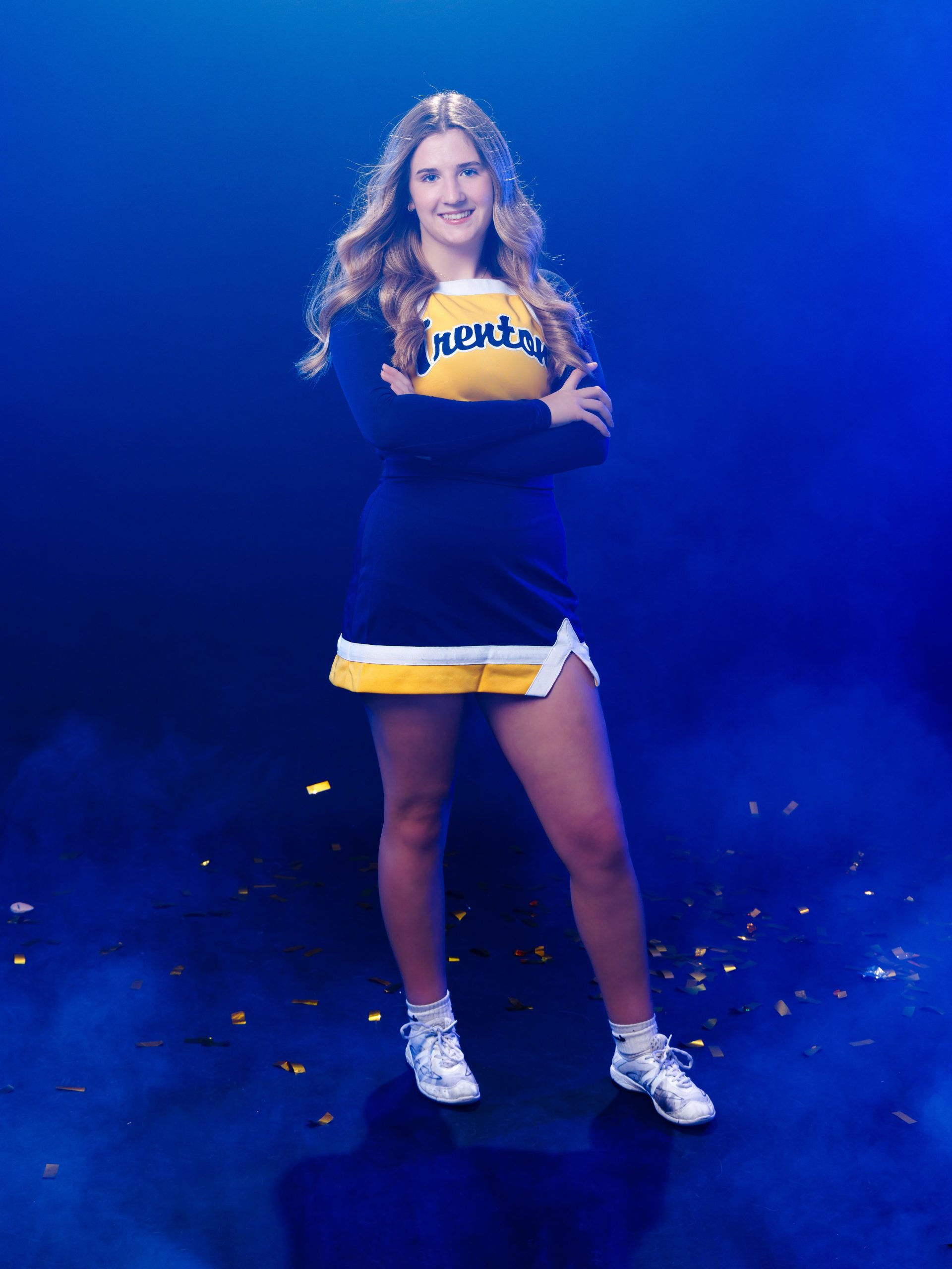 Cheerleader posing with hand on hip against blue backdrop with confetti