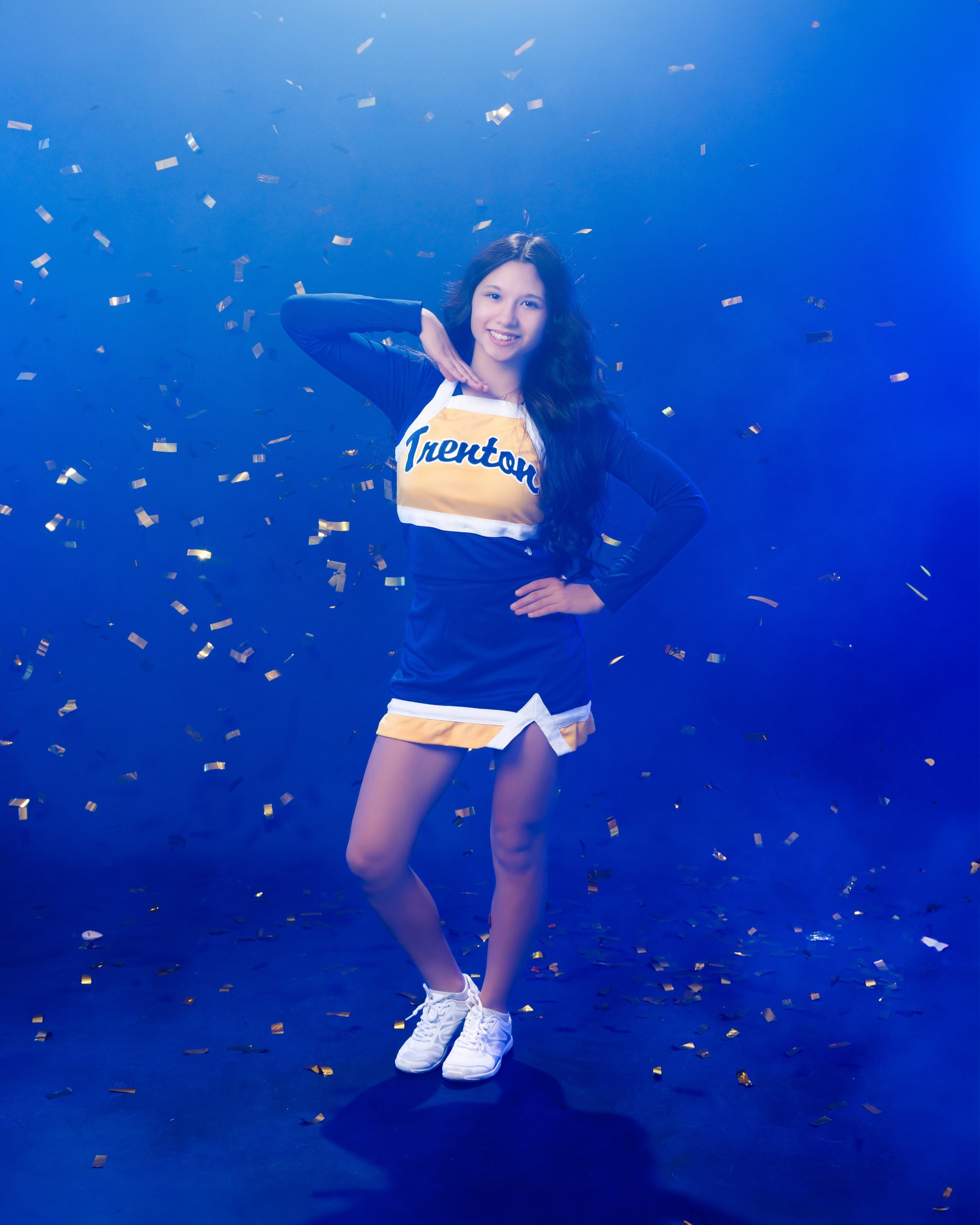 Cheerleader posing with hand on hip against blue backdrop with confetti