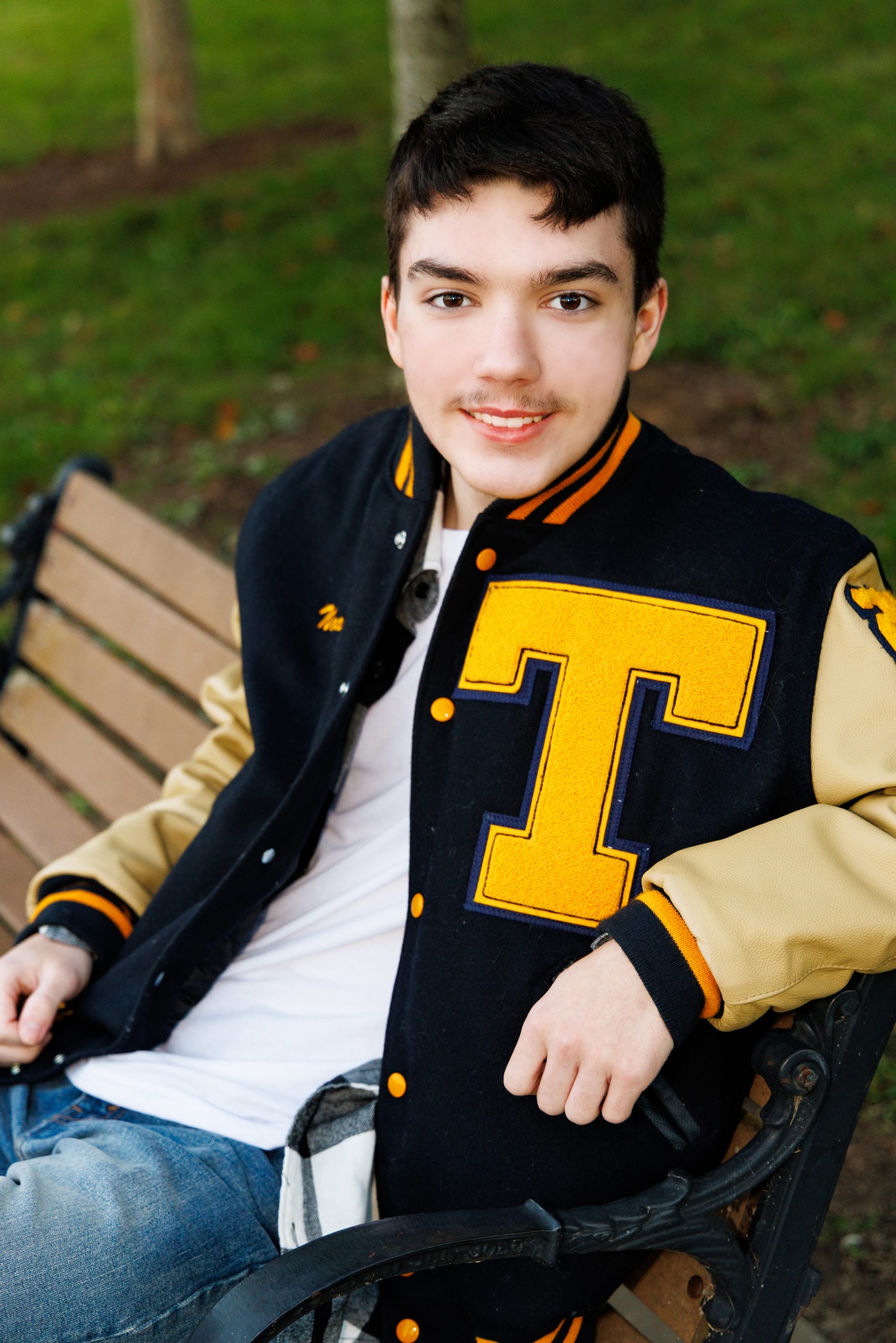 Student sitting on grass with fallen leaves during a senior photo session at Elizabeth Park, Trenton