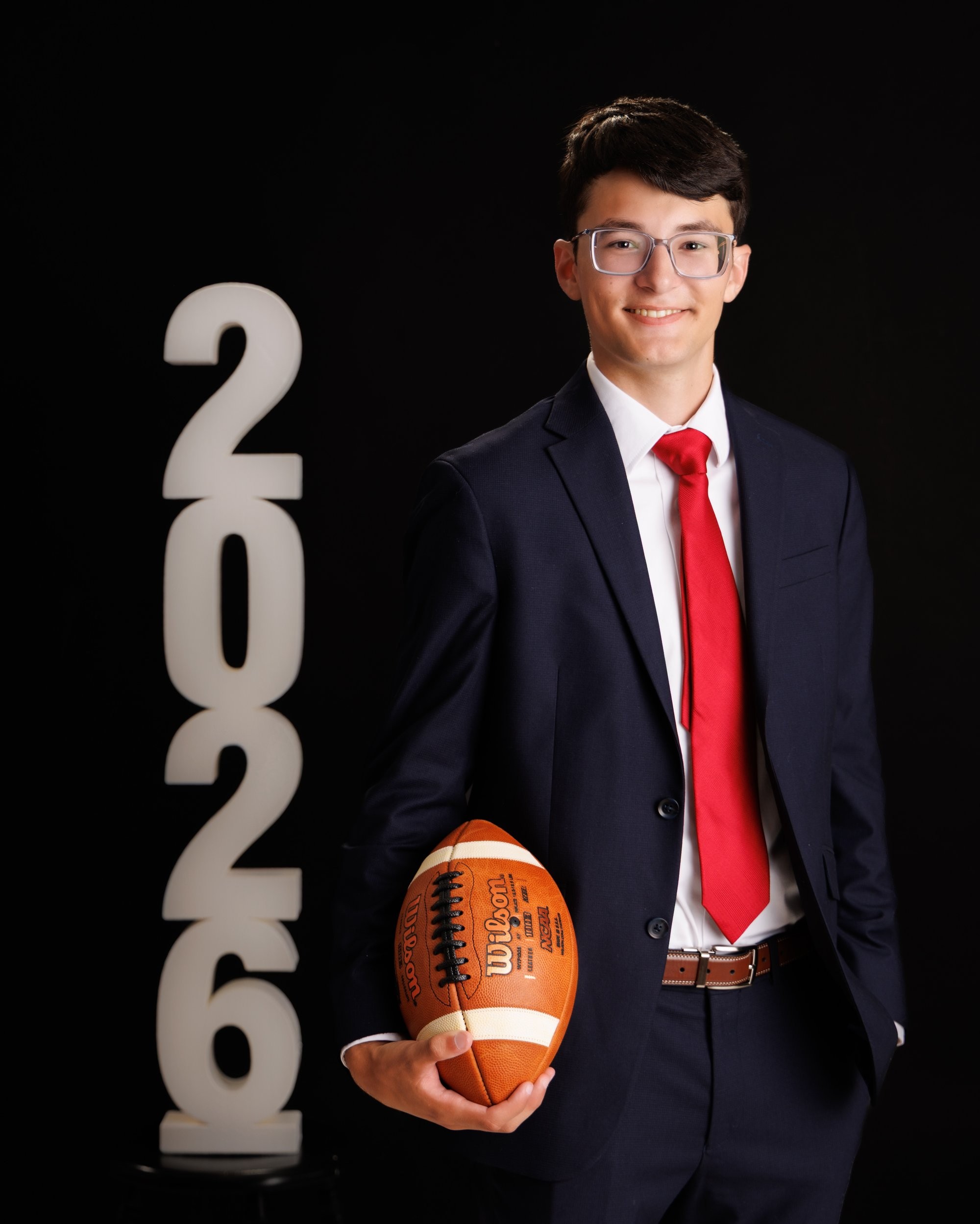 Anthony holding an American football while dressed in a navy suit and red tie for his Trenton senior portrait