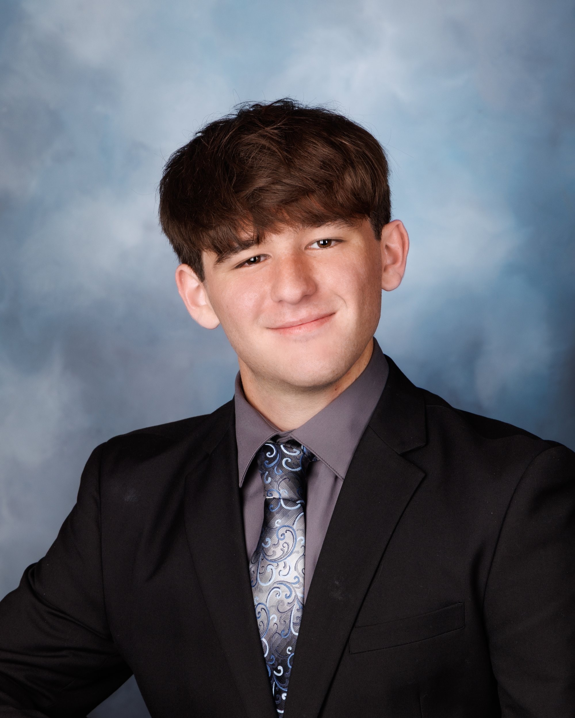 Dynamic senior photo of Khalan in a dark setting, dressed in a black suit and patterned tie for Trenton 2026 photography session