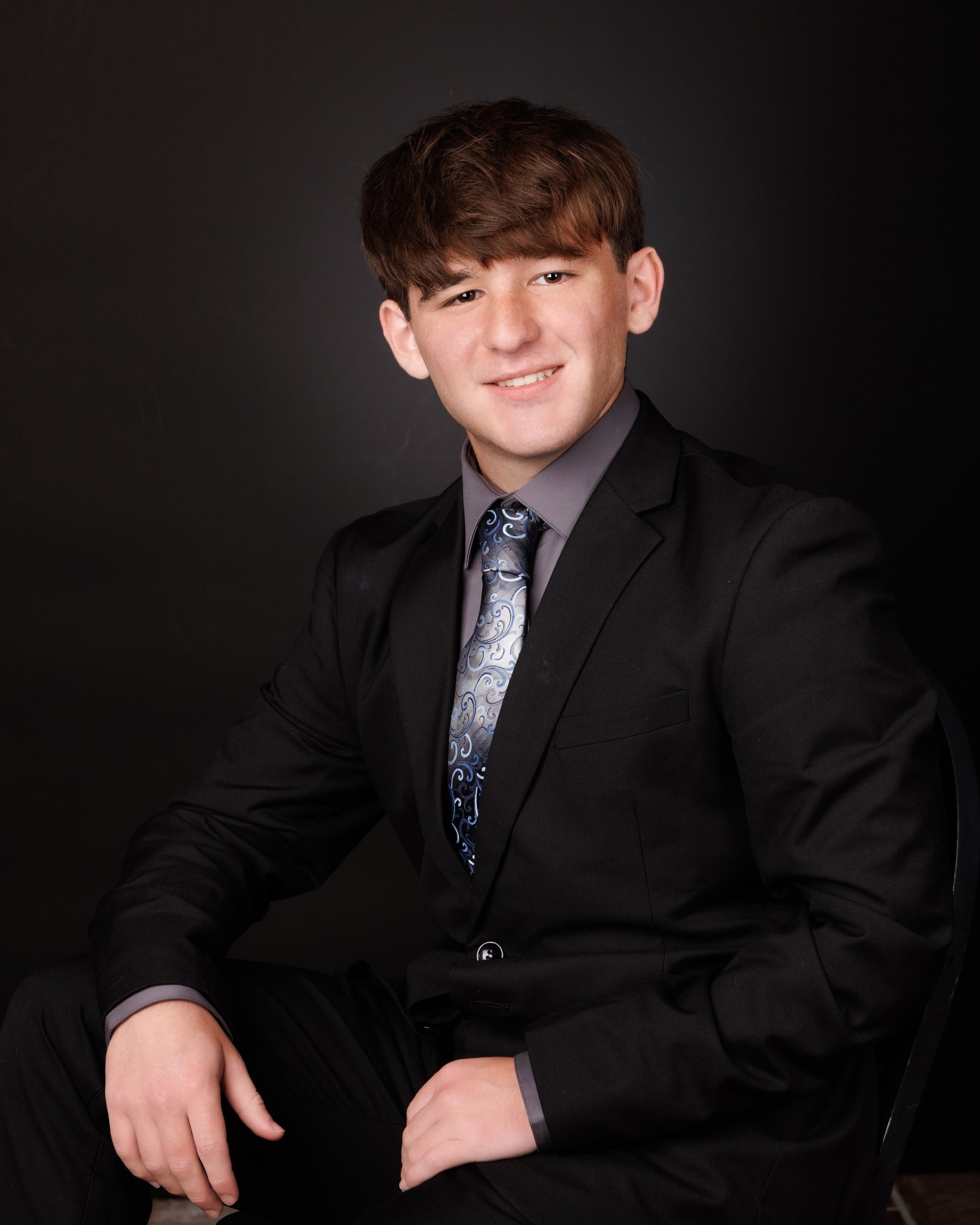 Dynamic senior photo of Khalan in a dark setting, dressed in a black suit and patterned tie for Trenton 2026 photography session