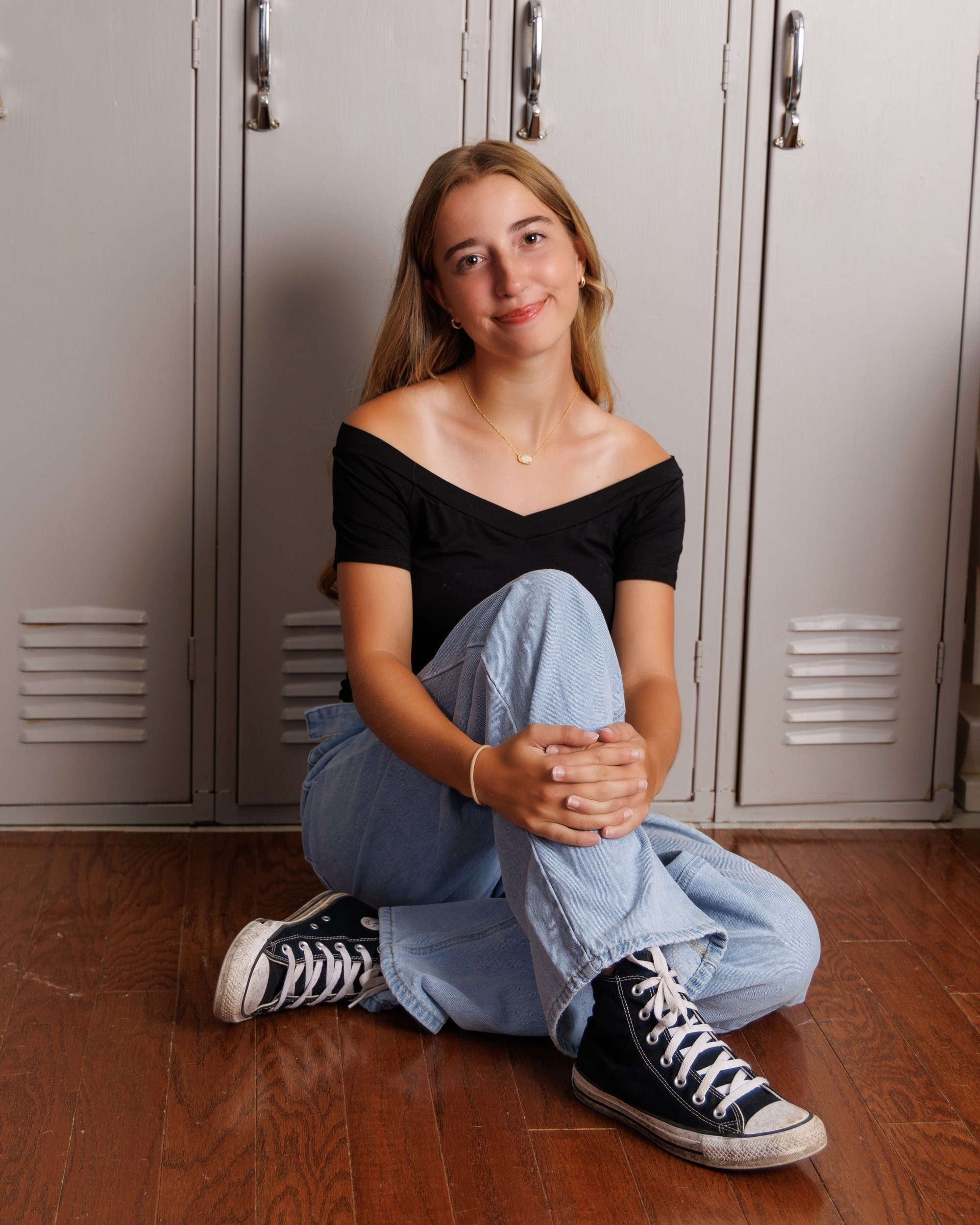 Senior portrait of Anika seated against lockers, showcasing casual style in a Trenton studio session