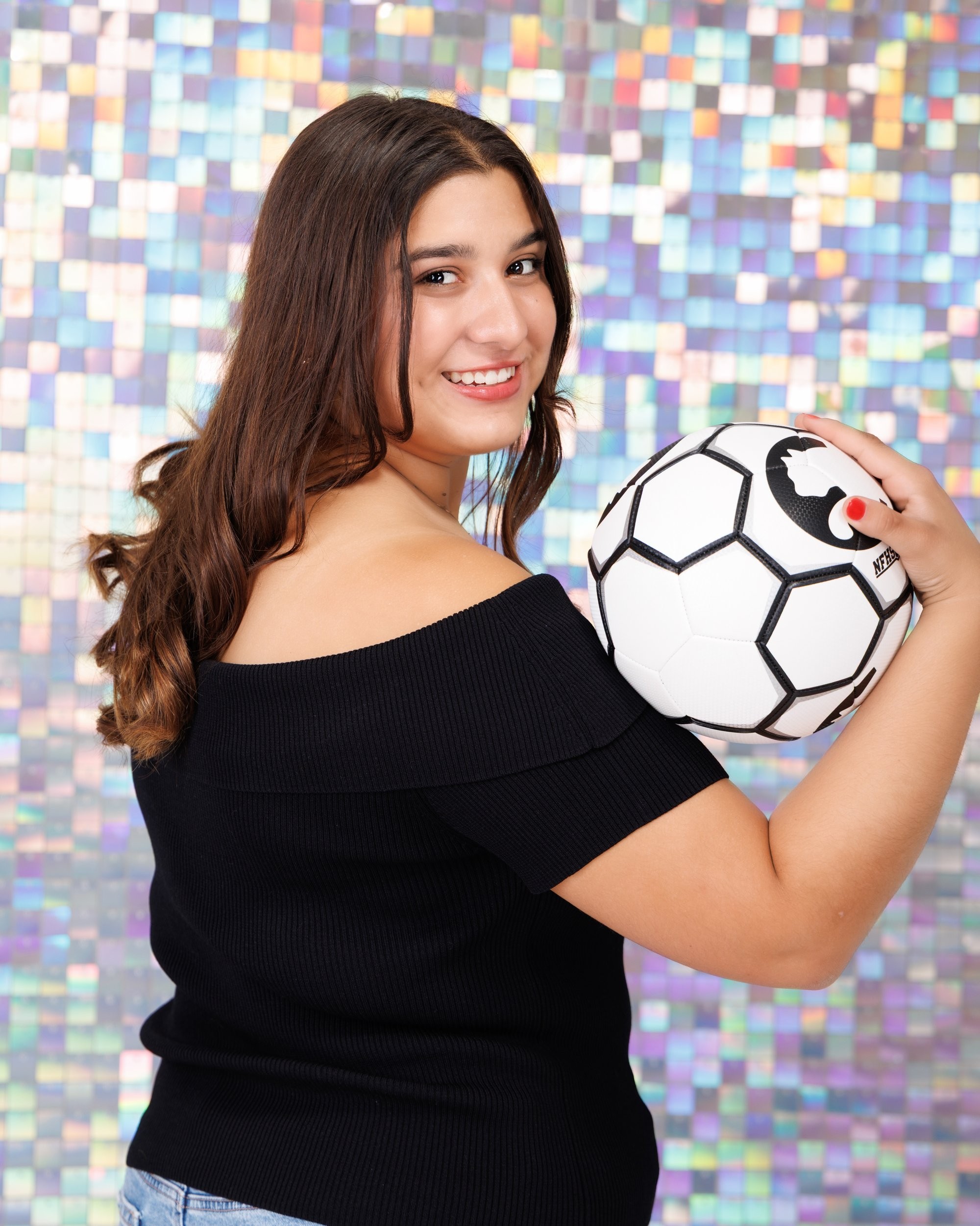 Back view of Ava holding a soccer ball in Trenton senior photo session, off-shoulder black top and mosaic wall