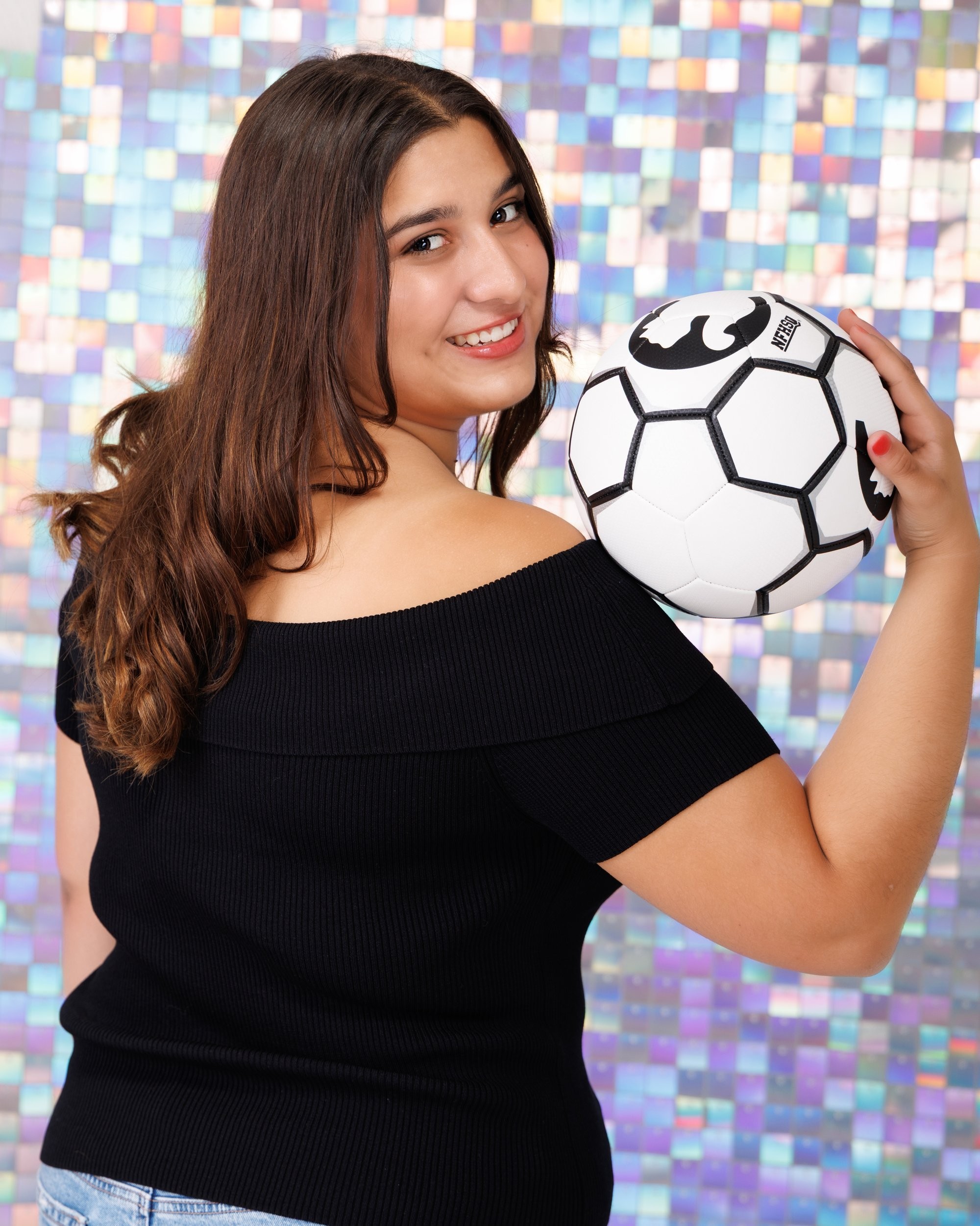 Back view of Ava holding a soccer ball in Trenton senior photo session, off-shoulder black top and mosaic wall