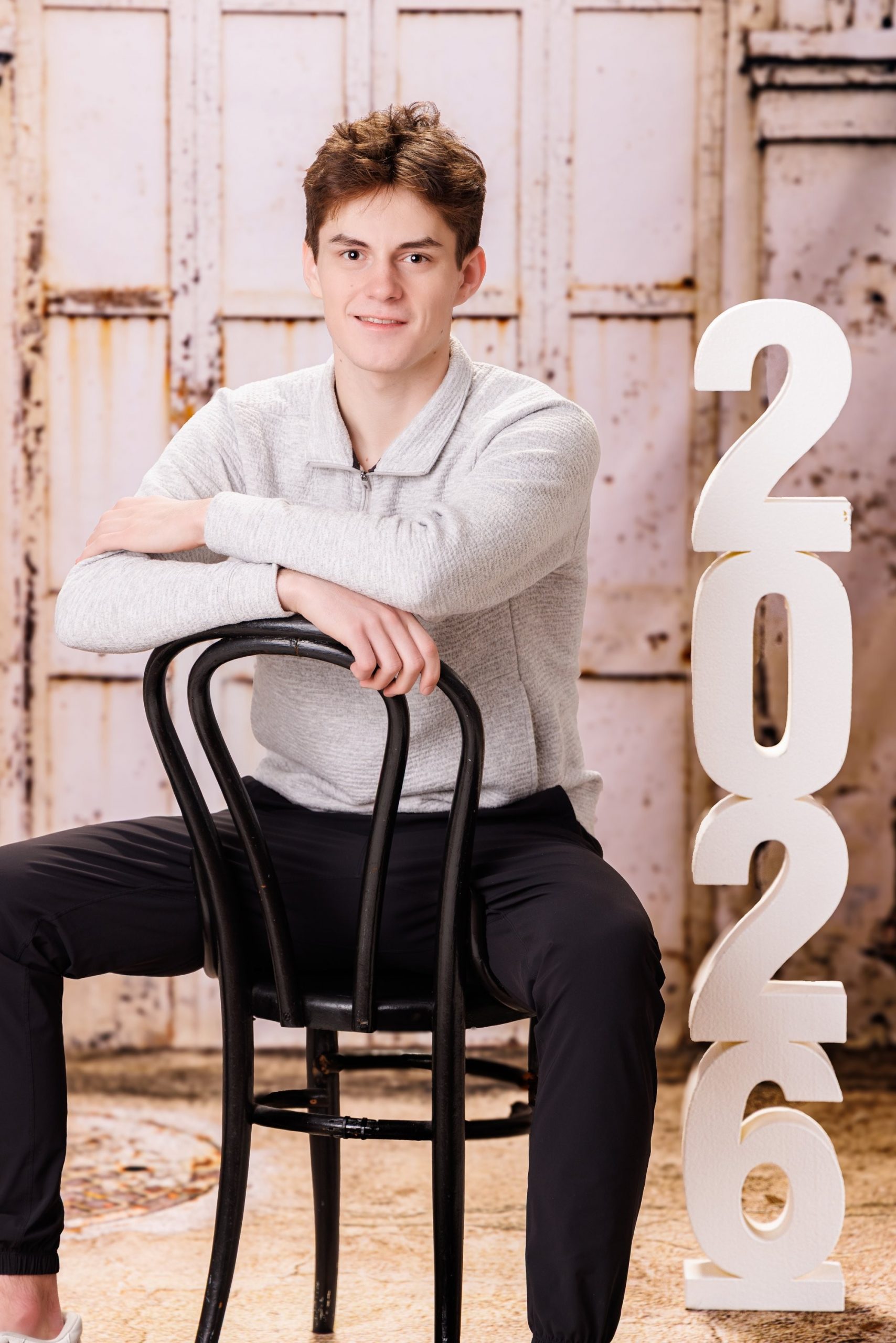 2026 milestone senior photo with the subject posed against a rustic background and large '2026' numerals