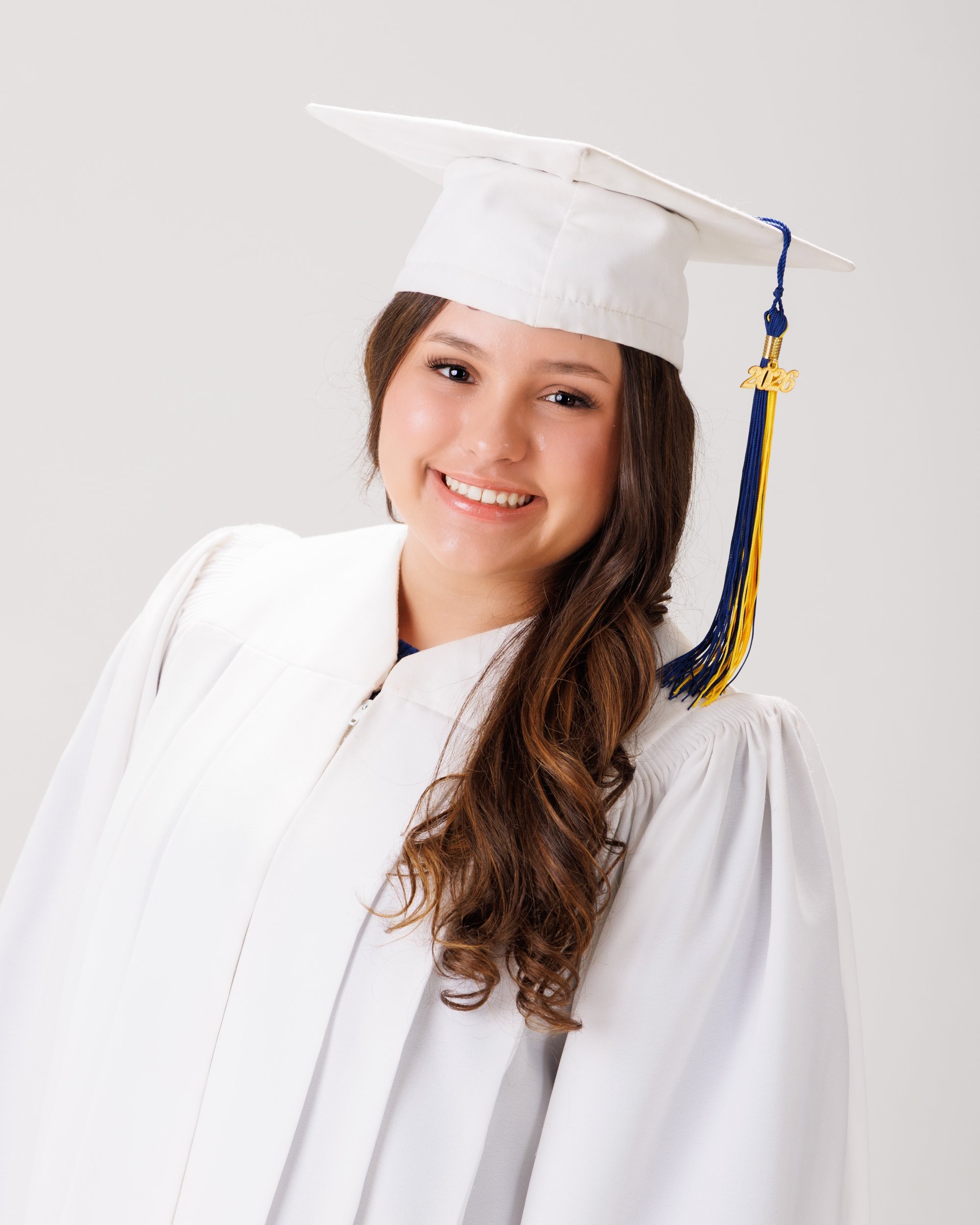 Student wearing graduation regalia with blue and gold pom-poms in a neutral backdrop for Trenton senior photography