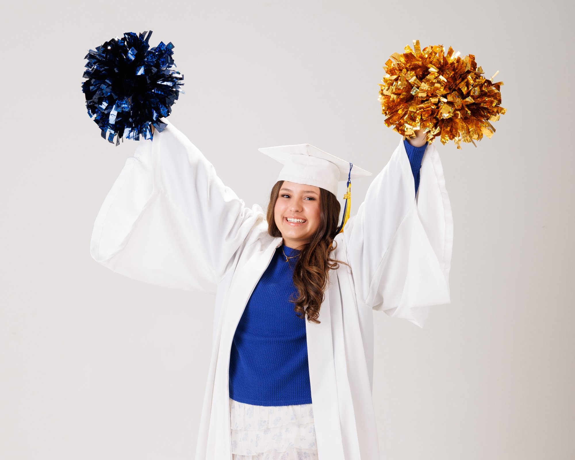 Student wearing graduation regalia with blue and gold pom-poms in a neutral backdrop for Trenton senior photography